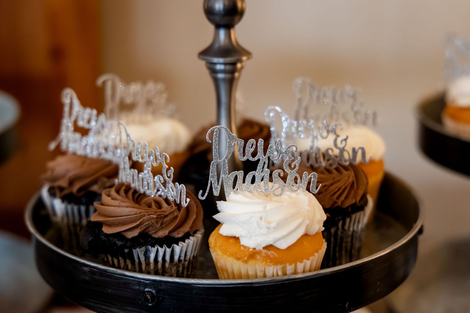 Wedding cupcakes with personalized name toppers reading Drew and Madison on tiered silver stand.
