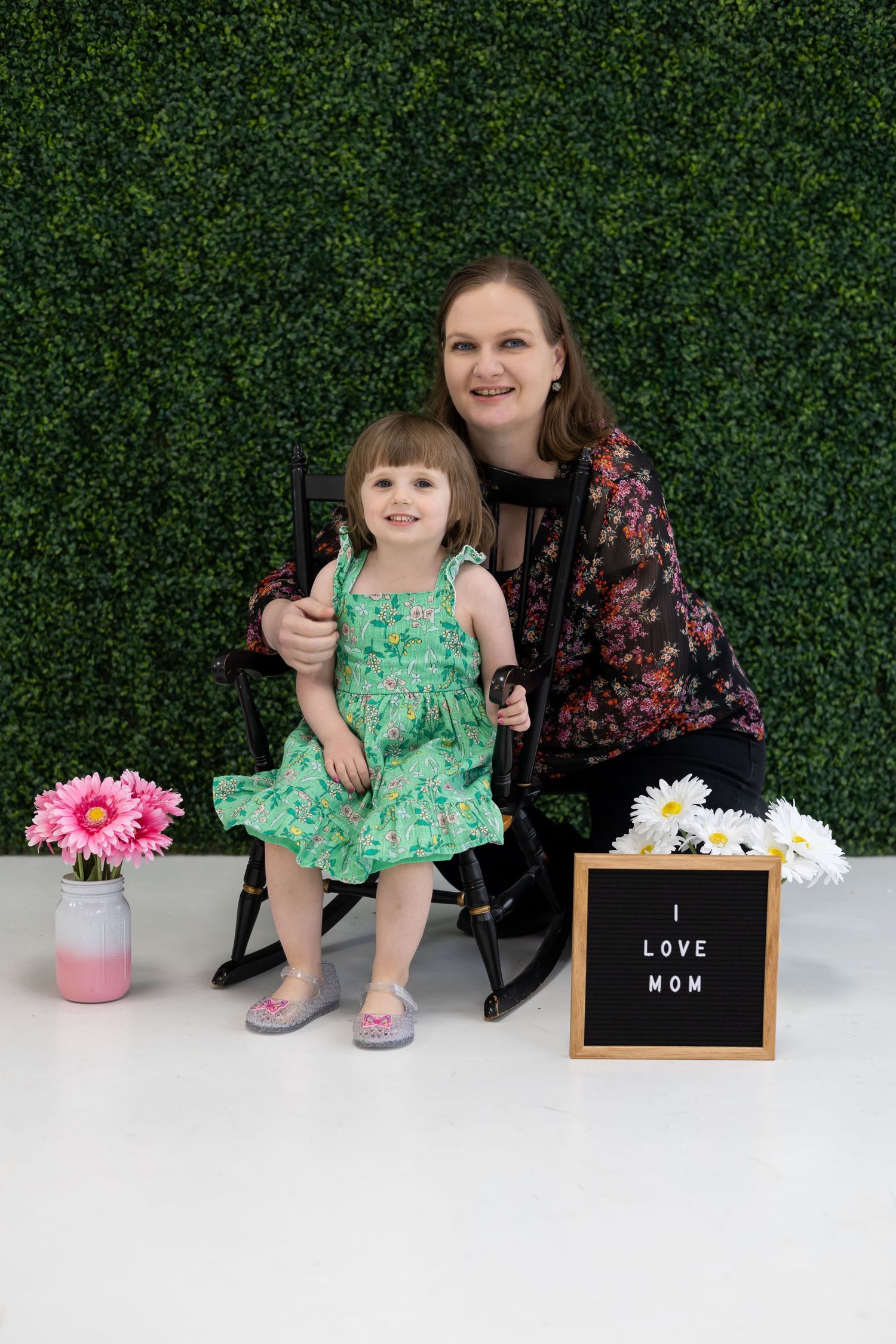 A mother-daughter portrait with spring decor including flowers and a 'Love Mom' sign.