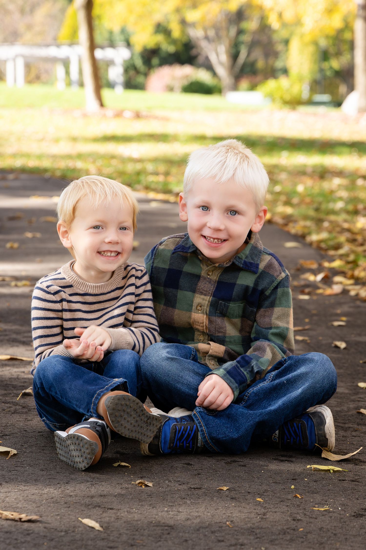 Two children sitting together on ground with fallen leaves sharing joyful moments.