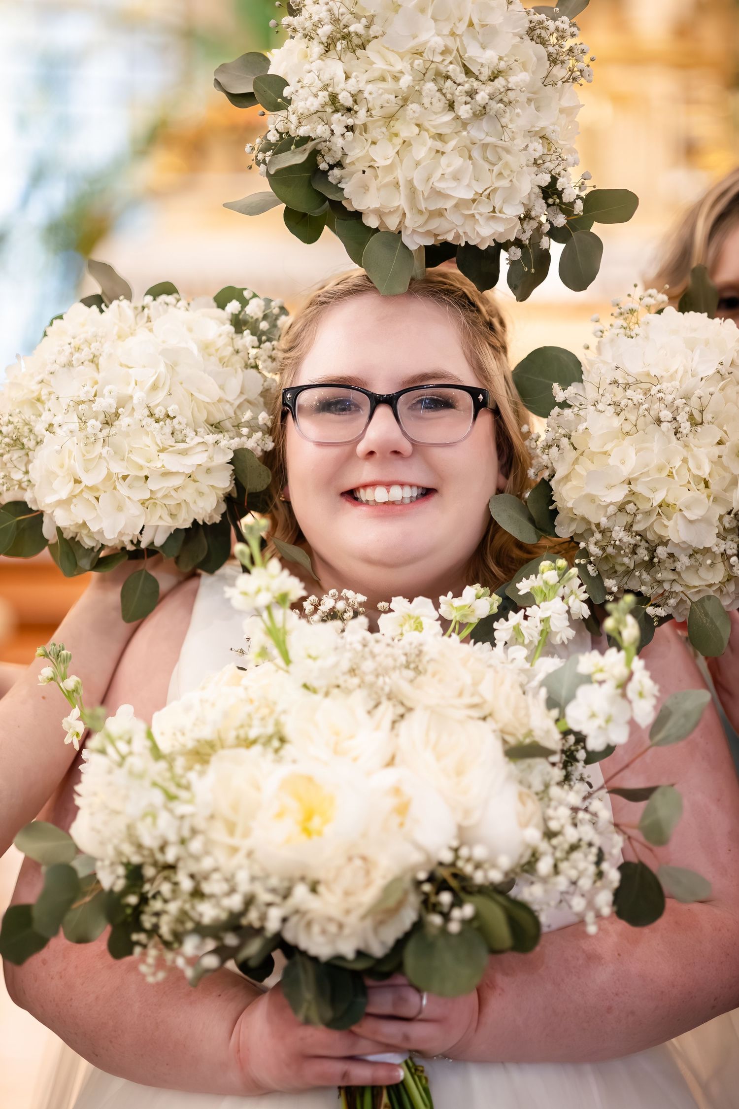 Smiling bride with glasses surrounded by white hydrangea and peony bouquets held by bridesmaids.