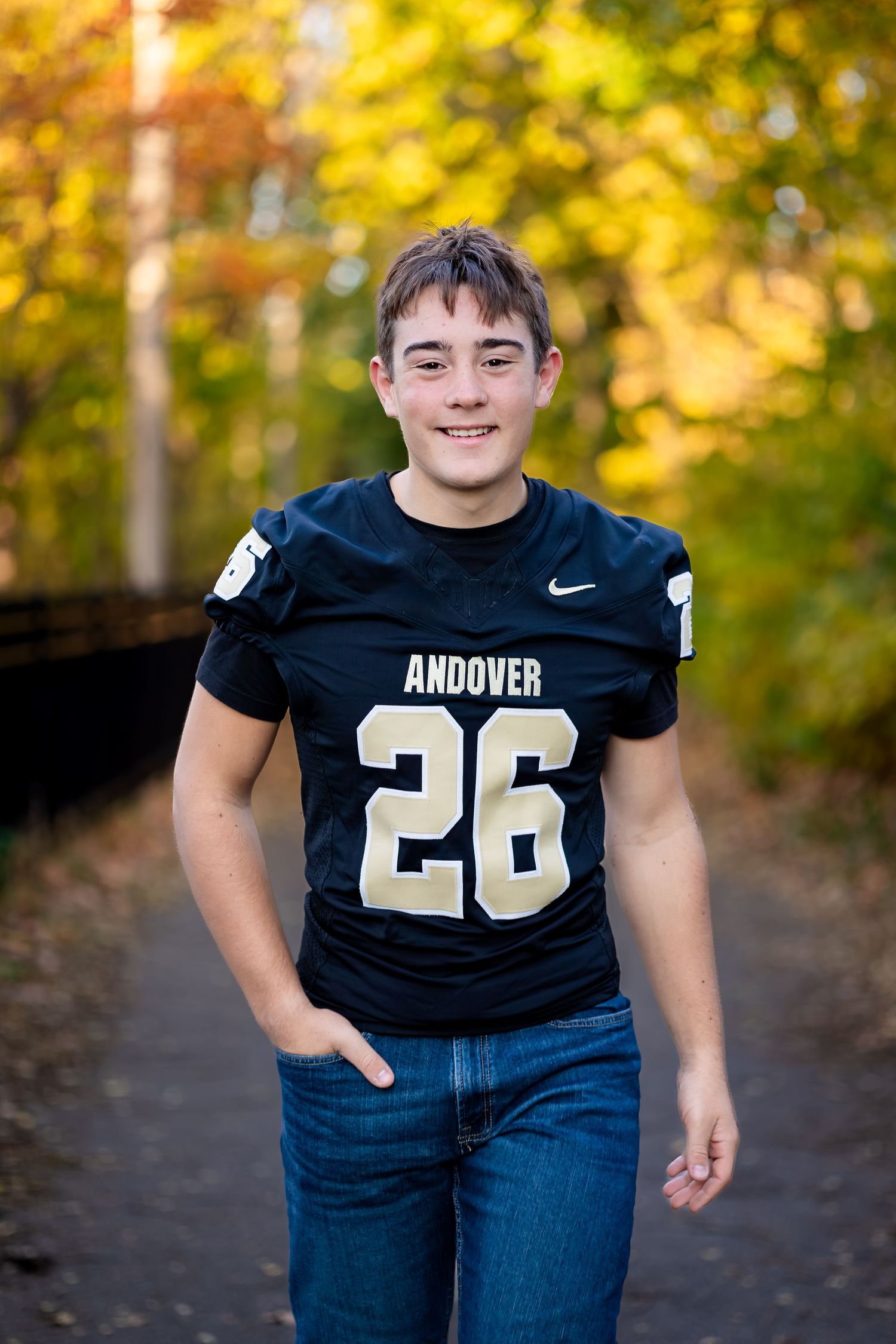 Athletic figure in black Andover jersey number 26 poses against vibrant fall foliage background.
