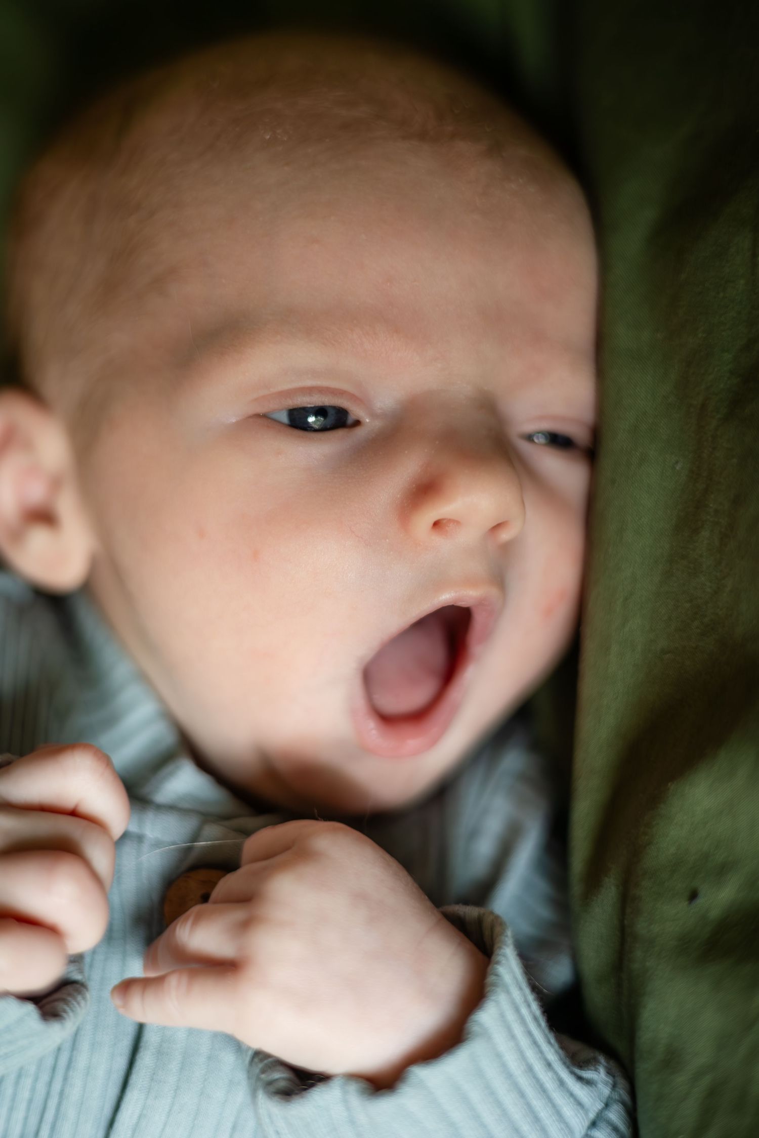 Baby making expressive face while lying on green bedding.