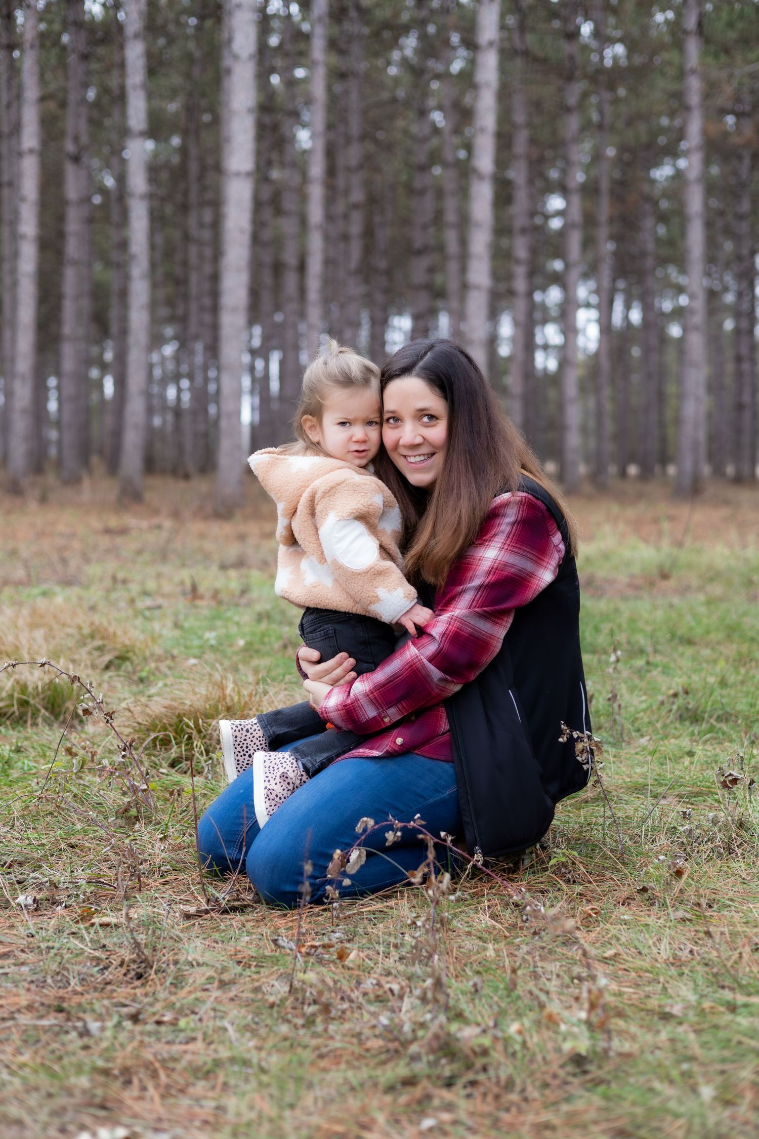 A tender moment between parent and child sitting in a pine forest clearing.