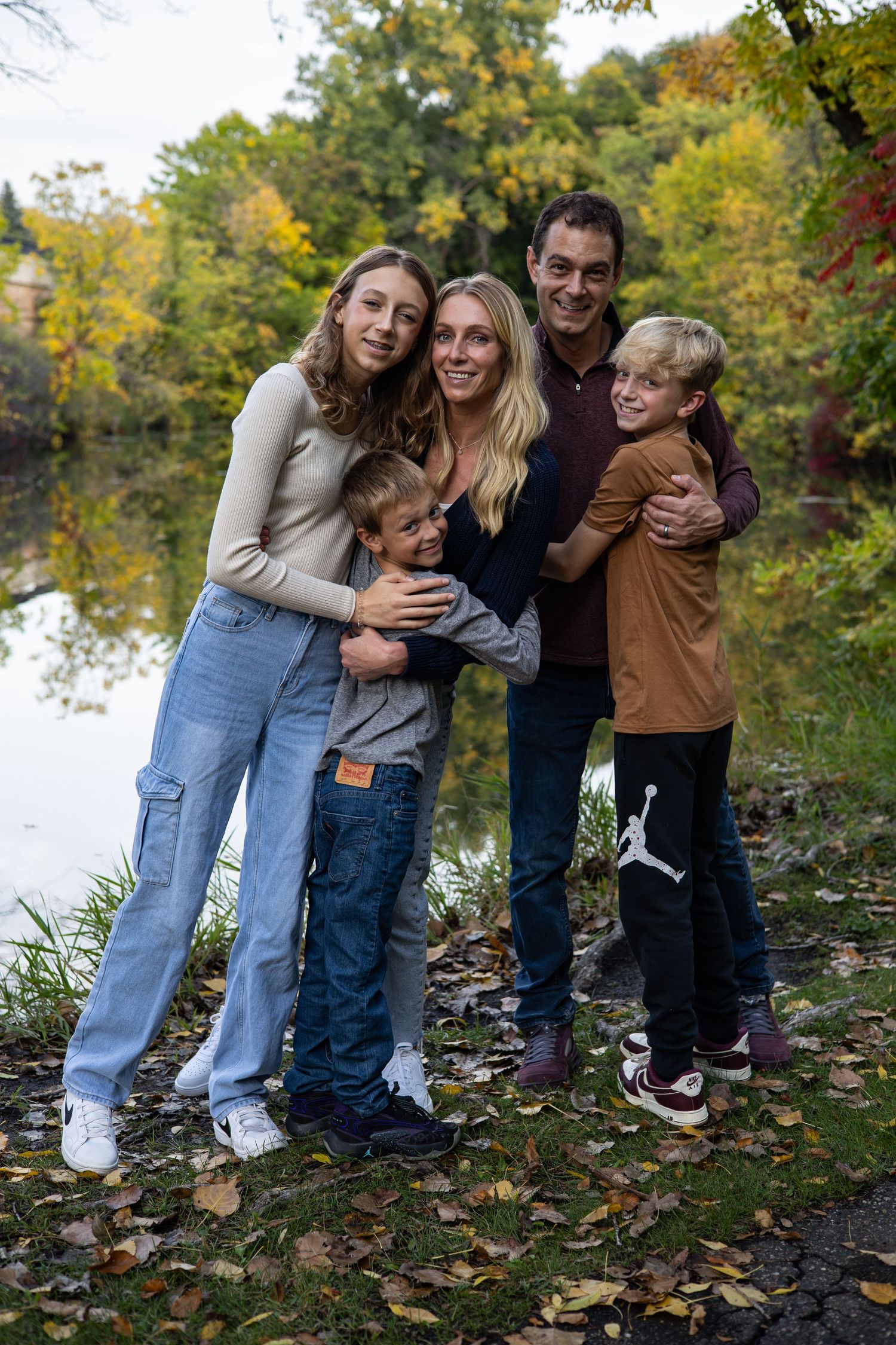 Playful family embracing and laughing by autumn lake.