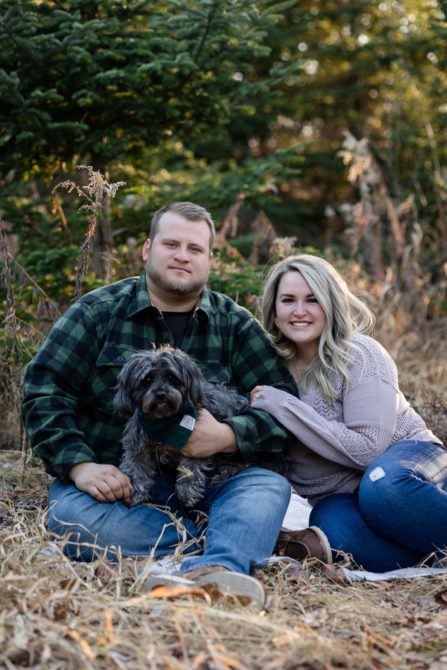 A couple relaxing outdoors with their black dog on fallen leaves during an autumn photoshoot.