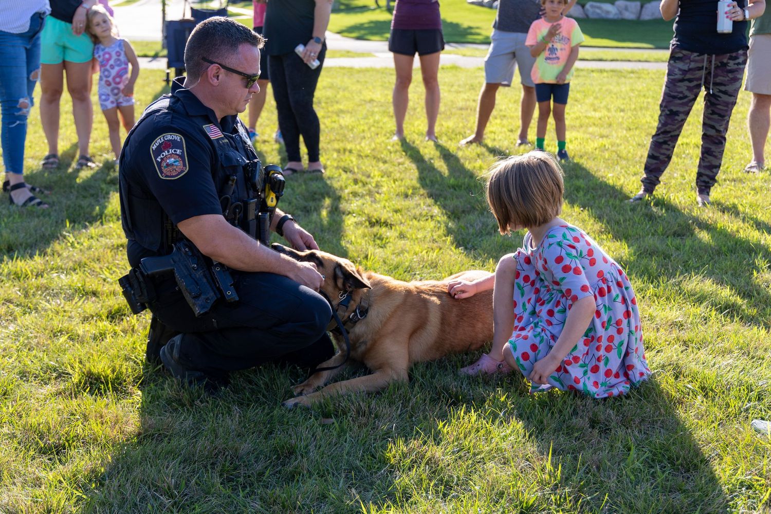 Police K-9 unit interacts with community members on grass field during public event.