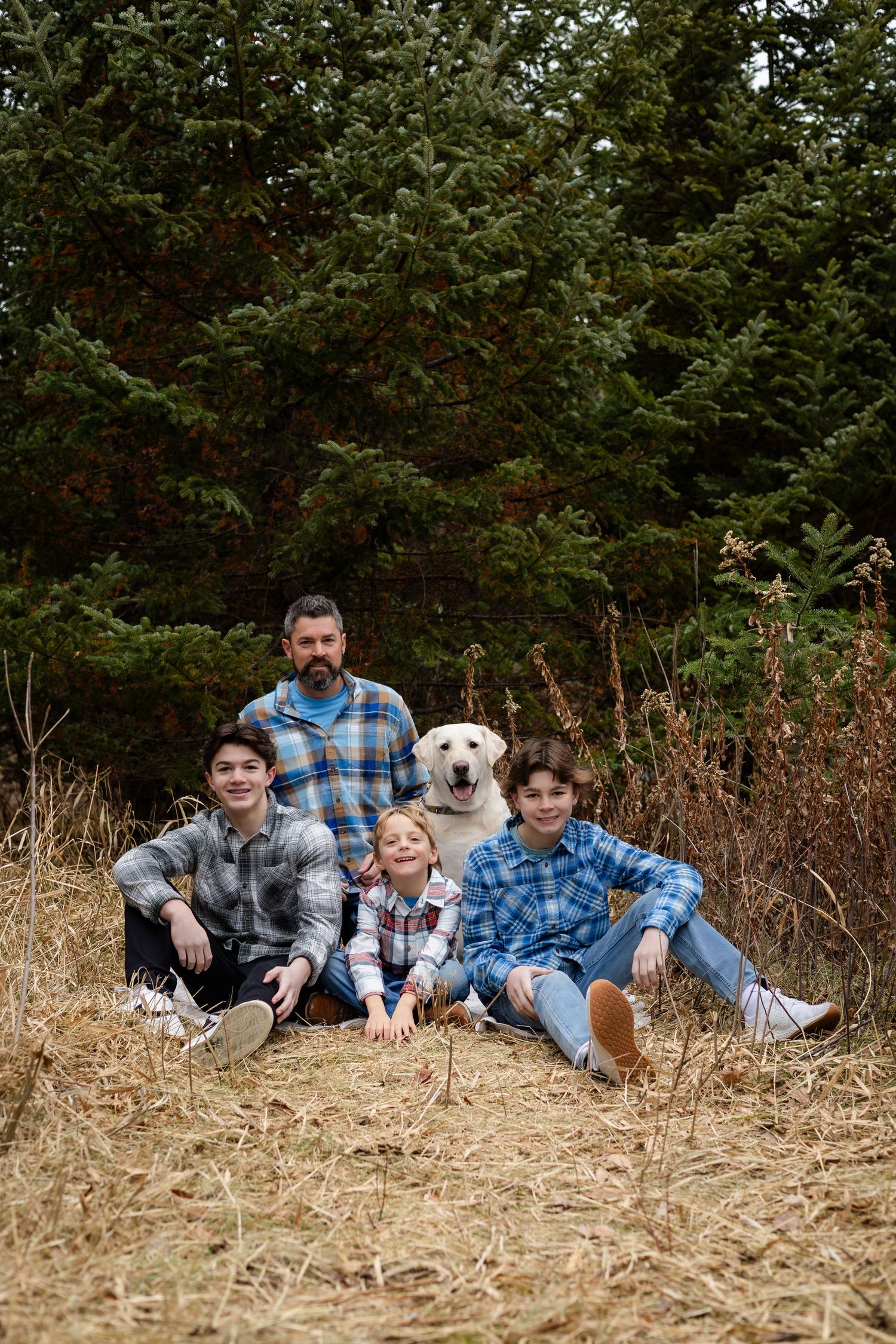A casual group portrait of people relaxing in dried grass with evergreen trees in the background.