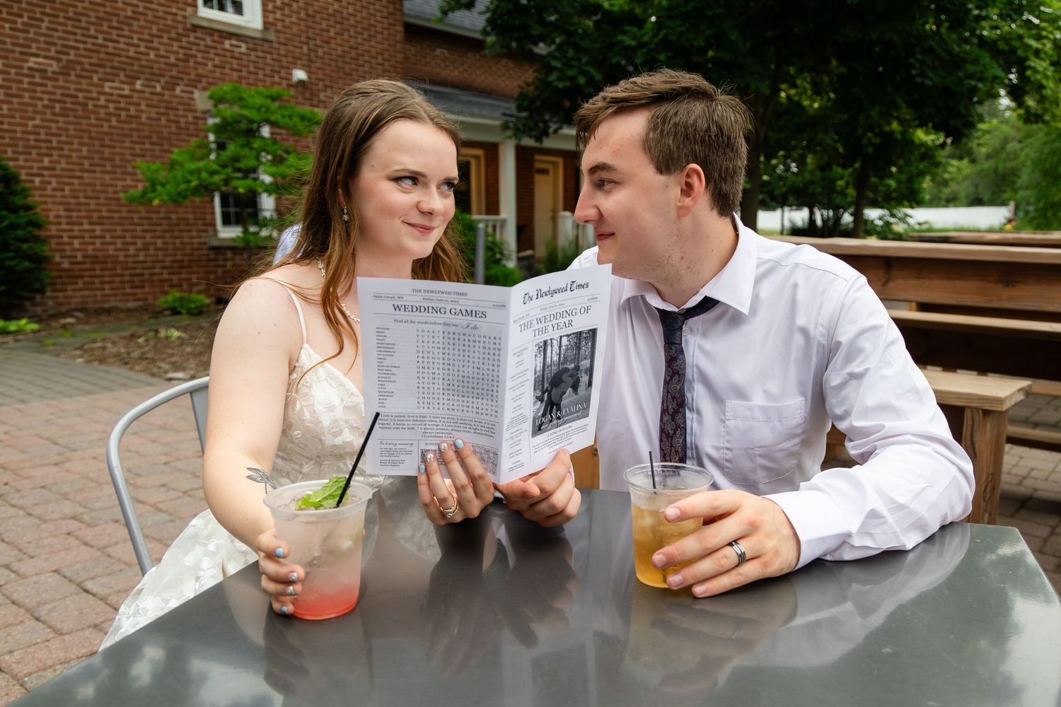 Wedding couple enjoys drinks at outdoor table during reception celebration.