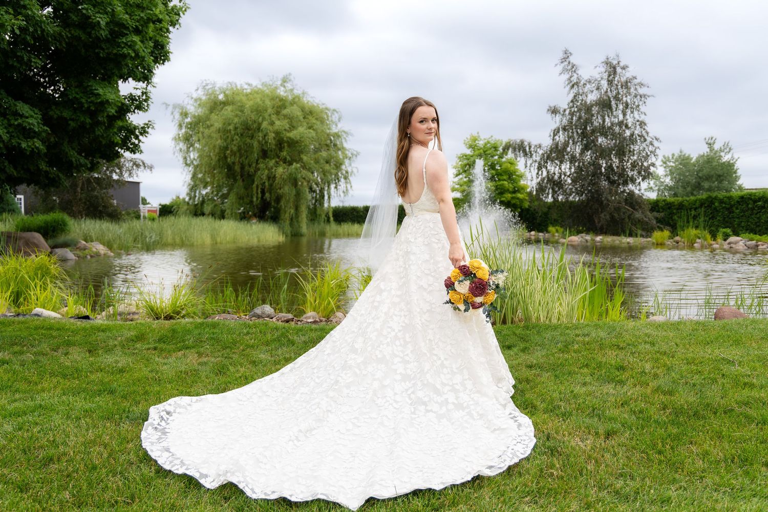 A bride in a white gown poses in an outdoor garden setting with natural greenery.