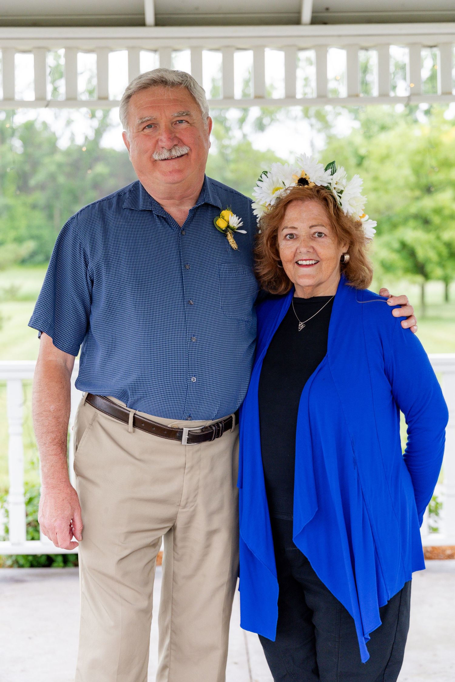 A couple smiles for a portrait on a covered porch wearing coordinated blue and khaki outfits.