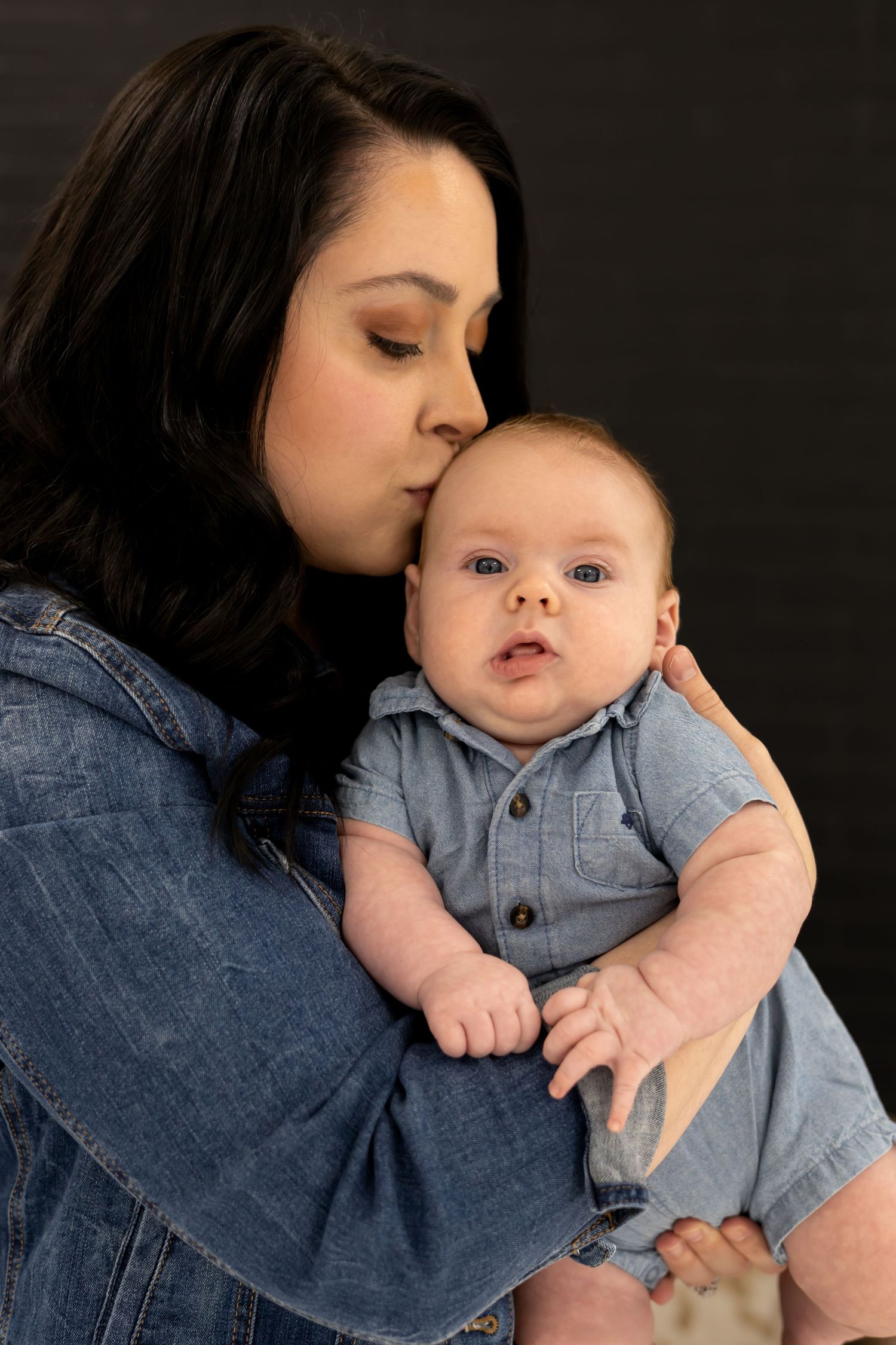 An intimate studio portrait showing a gentle moment between parent and infant in denim and blue.