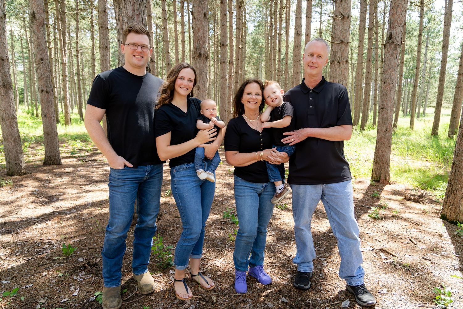 Group standing together in matching outfits in a sunlit pine forest.