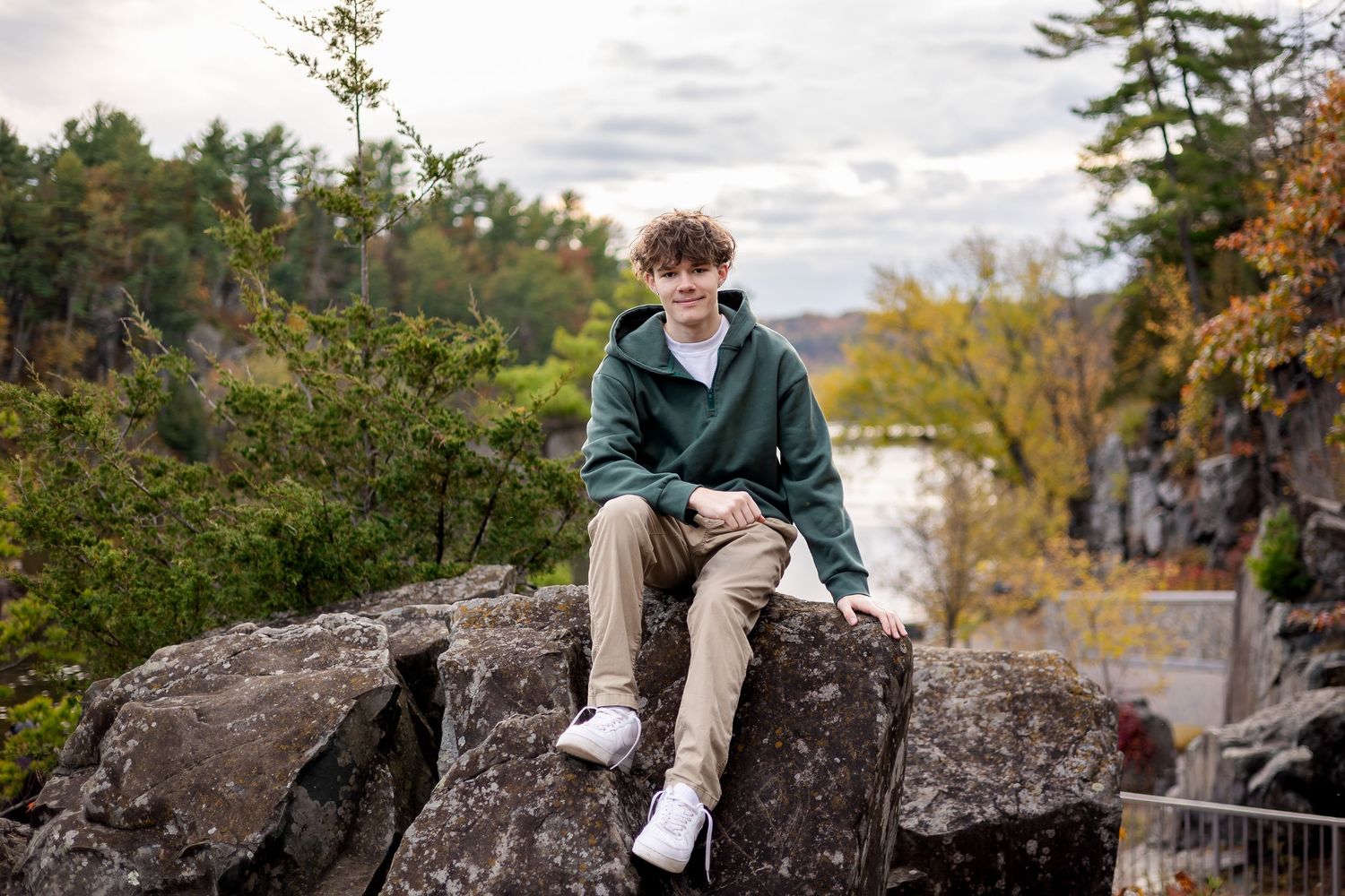 A person sits on large boulders surrounded by autumn foliage in a peaceful outdoor setting.