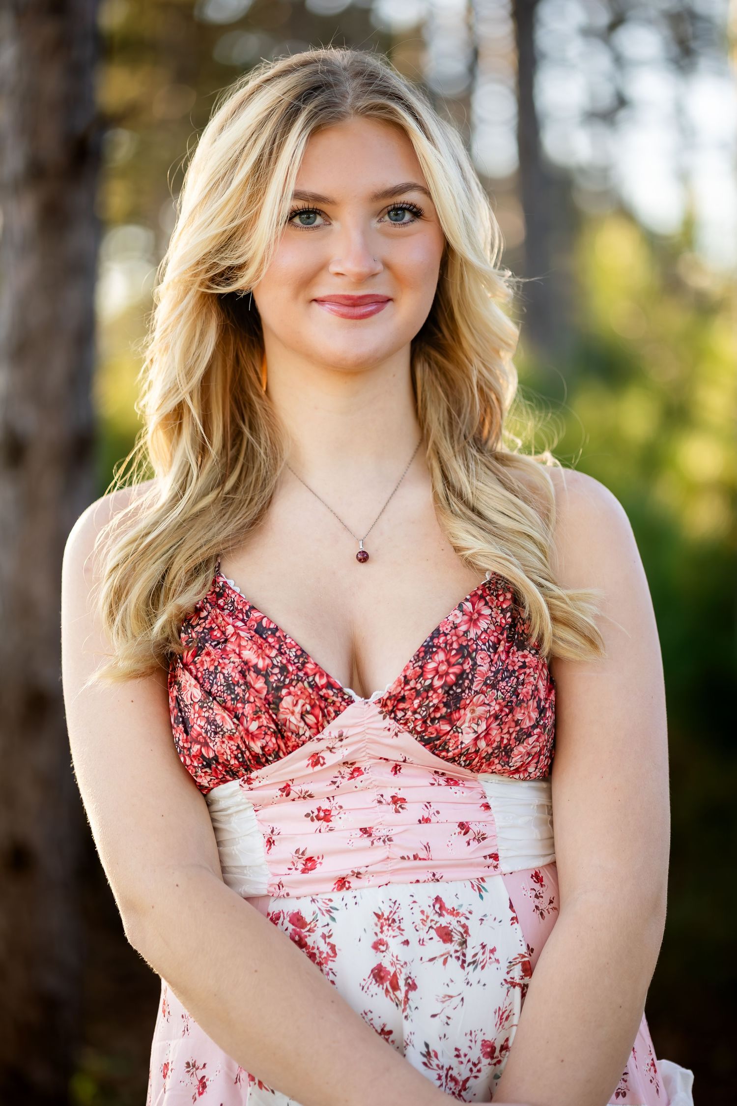 A portrait in a floral patterned dress with long blonde hair against a blurred forest background.