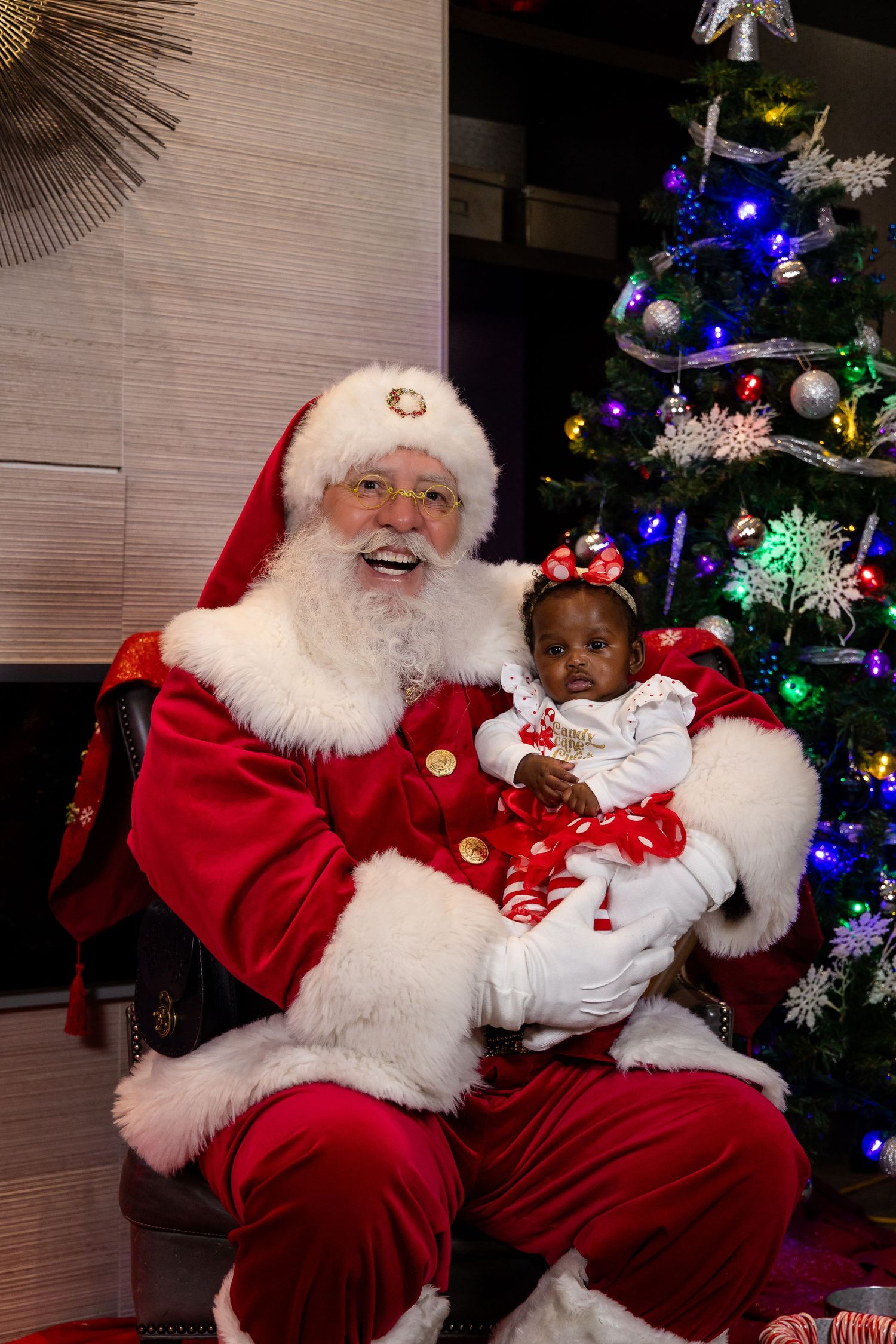 Santa Claus shares holiday cheer next to a brightly lit Christmas tree with colorful ornaments.