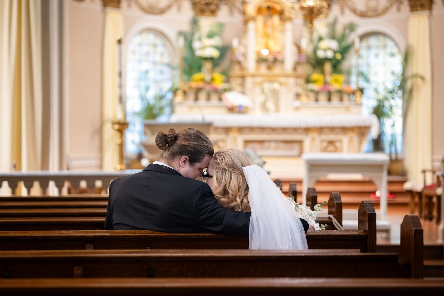 Bride and groom share an intimate moment together in a church pew during their wedding ceremony.