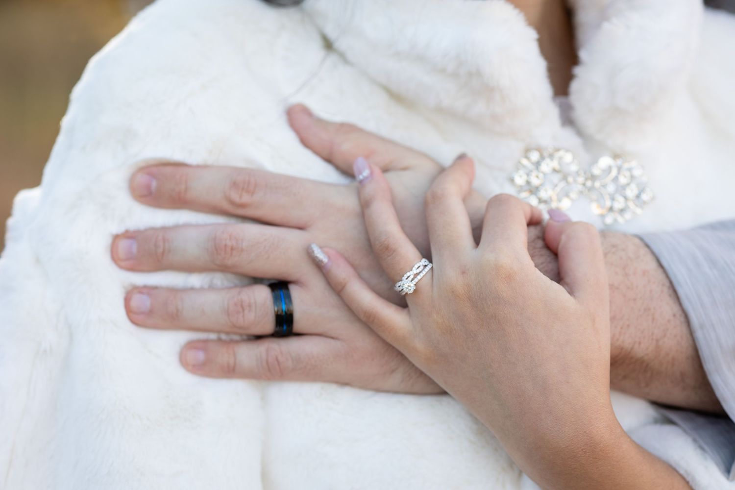 Close-up of hands displaying wedding rings against white fur fabric.