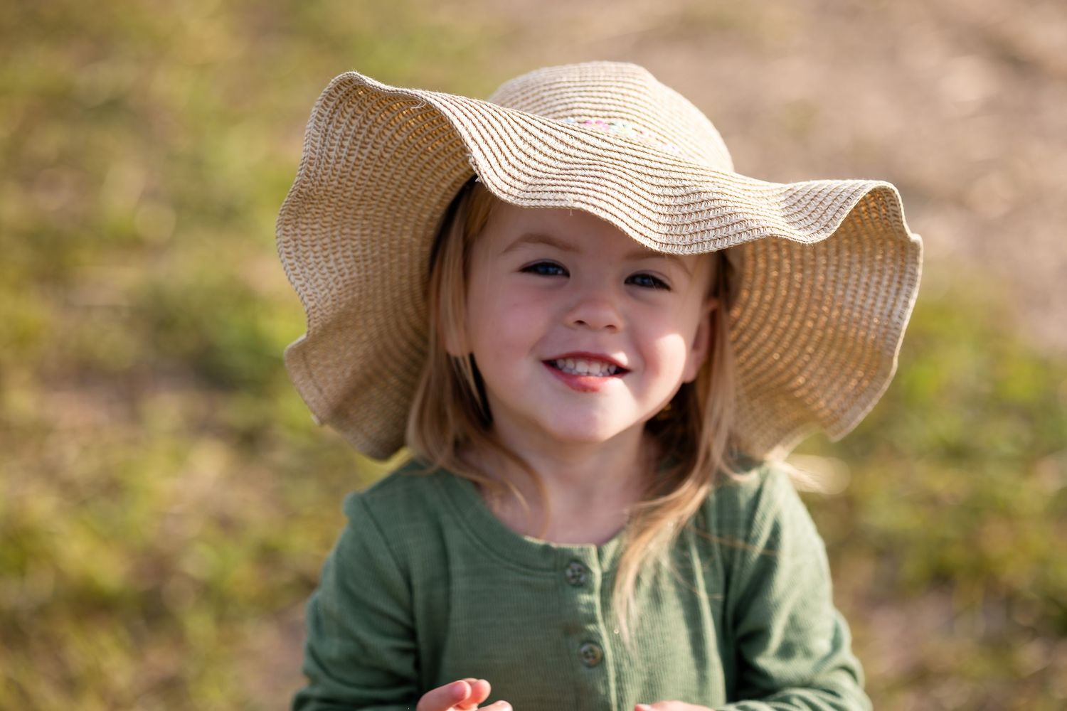 Child wearing straw sunhat and green sweater in outdoor setting.