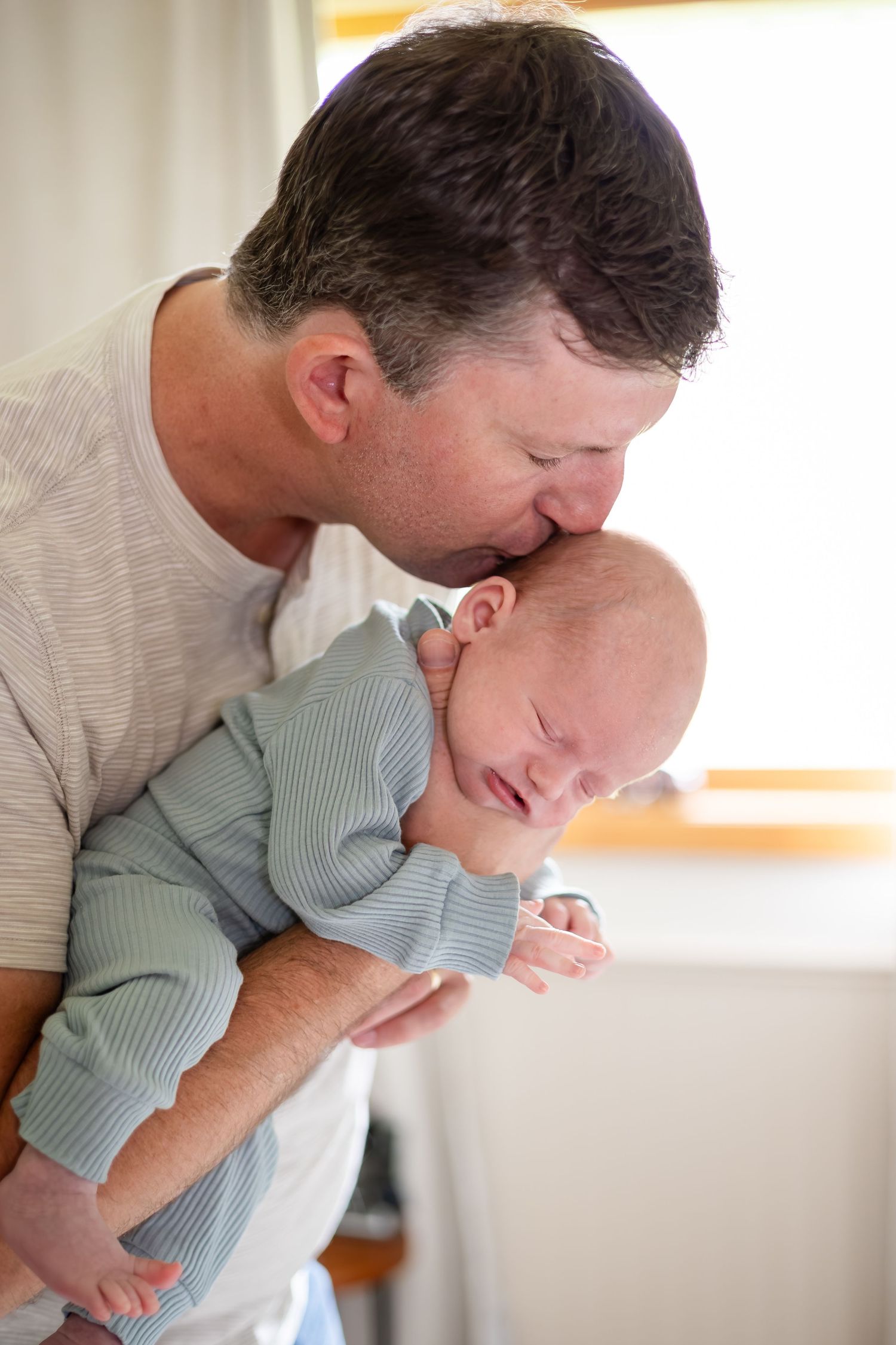 Parent holding and kissing a baby wearing a striped onesie in a tender moment.