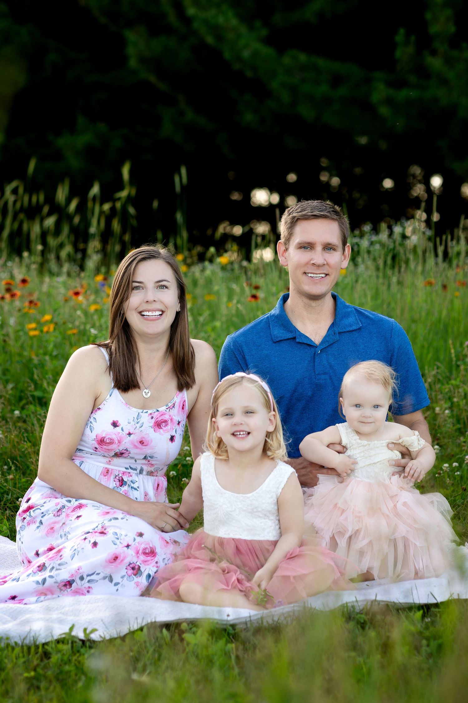 Family sitting together on blanket in wildflower meadow wearing coordinated summer outfits.
