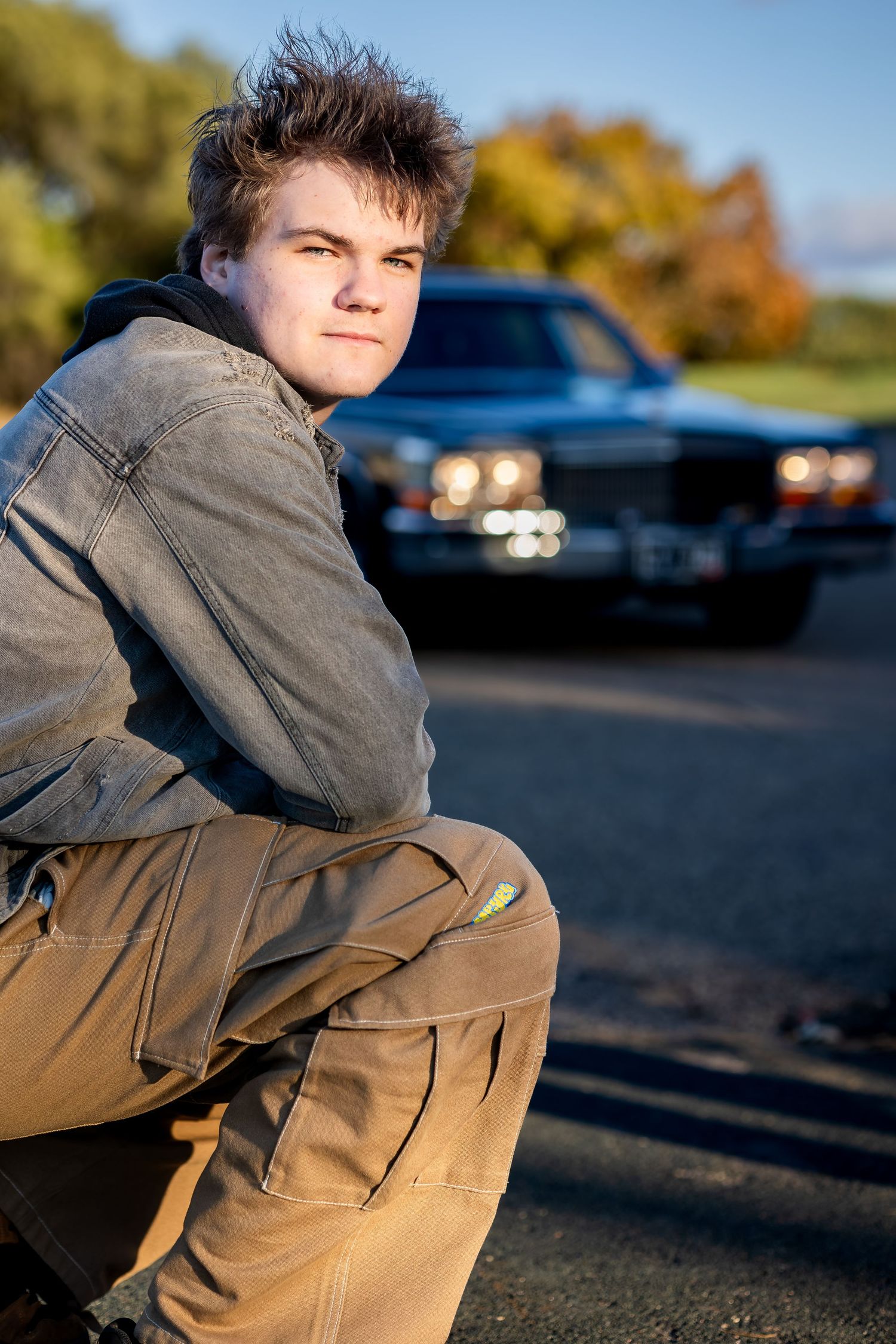 A casual portrait against a vintage car with autumn foliage in the background during golden hour.