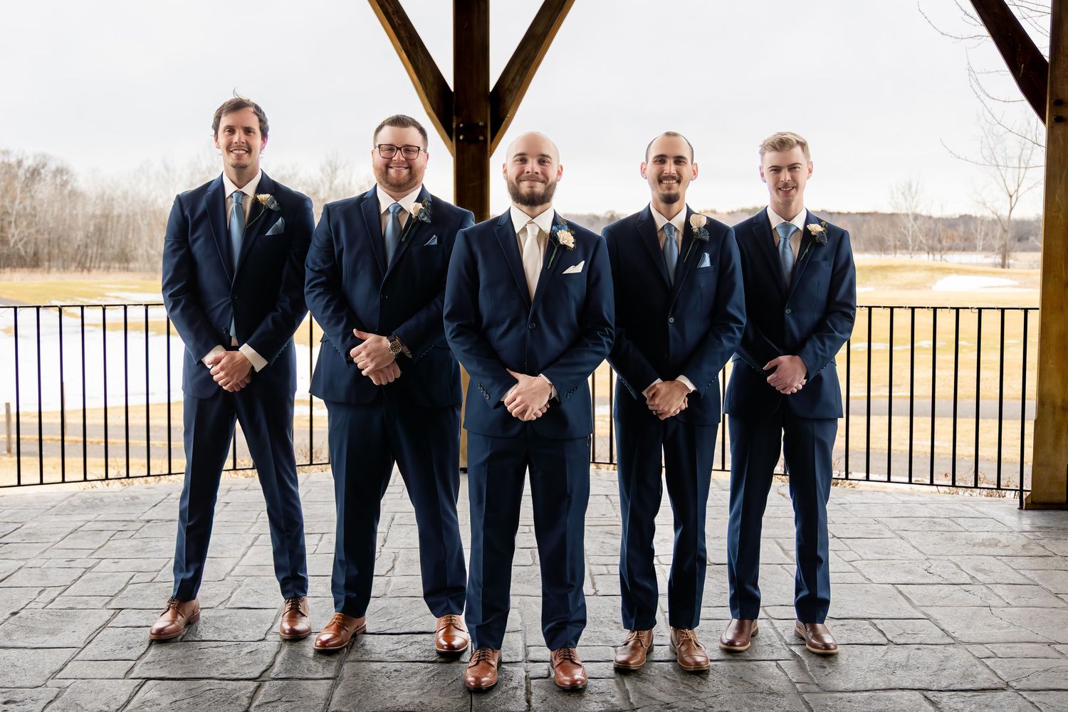 Groom and four groomsmen pose in matching navy suits on an outdoor patio.