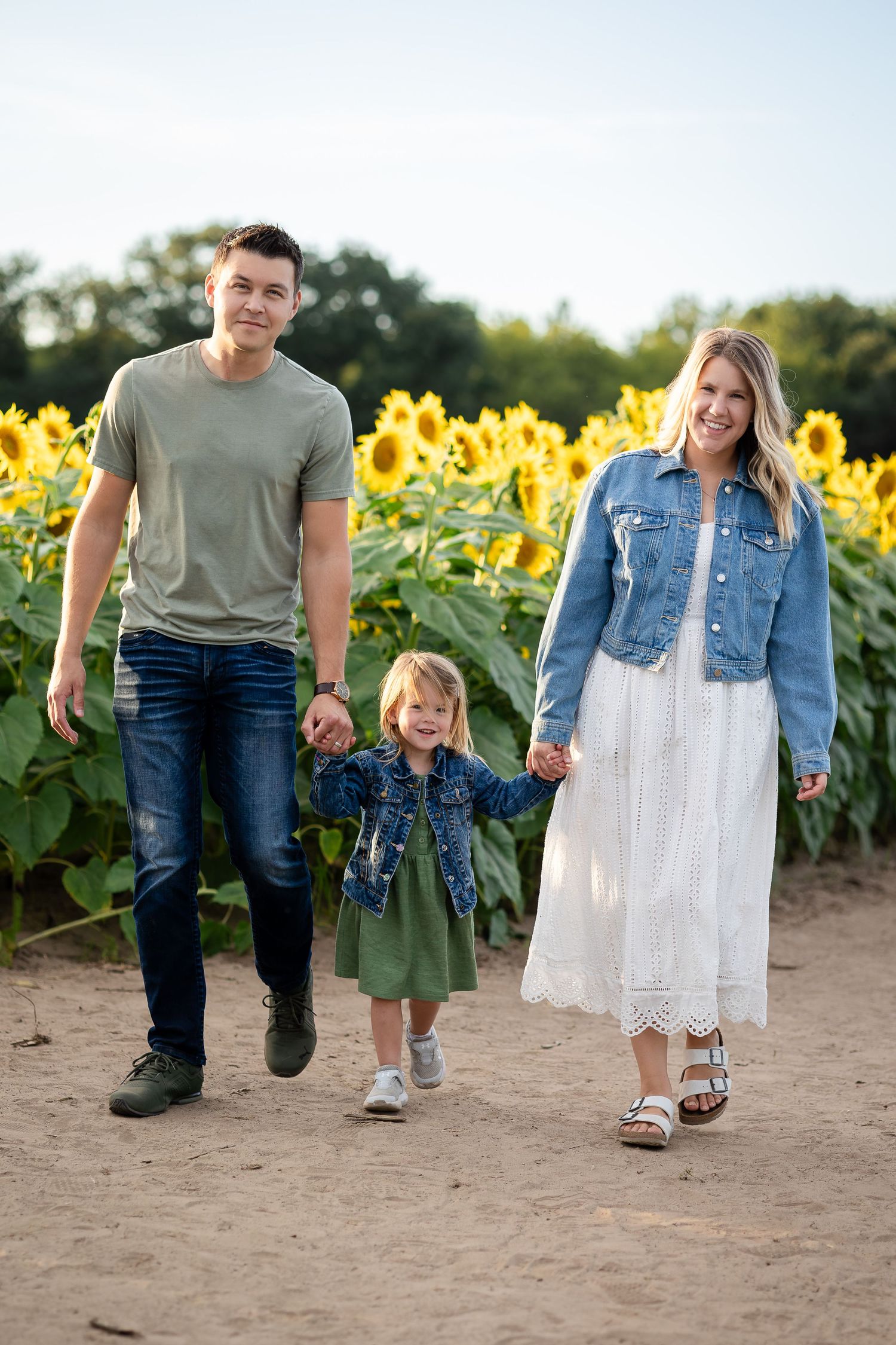 Family walking together through a dirt path surrounded by sunflowers.