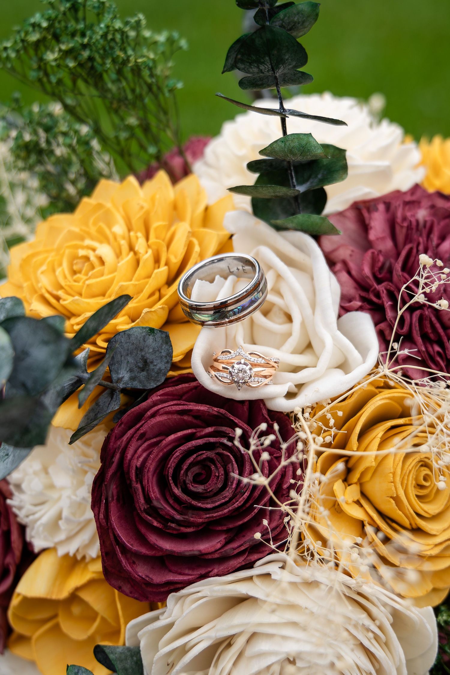 Wedding rings displayed on burgundy and yellow roses with white floral accents.