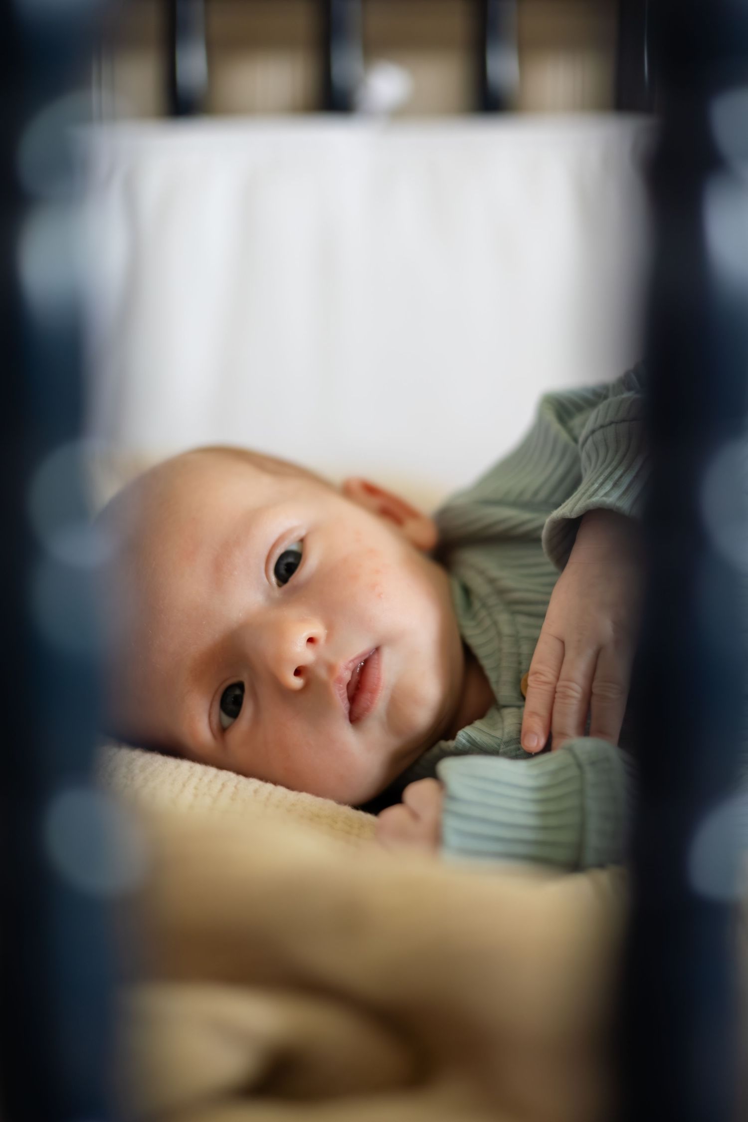 Baby lying in crib viewed through bars in dramatic lighting.