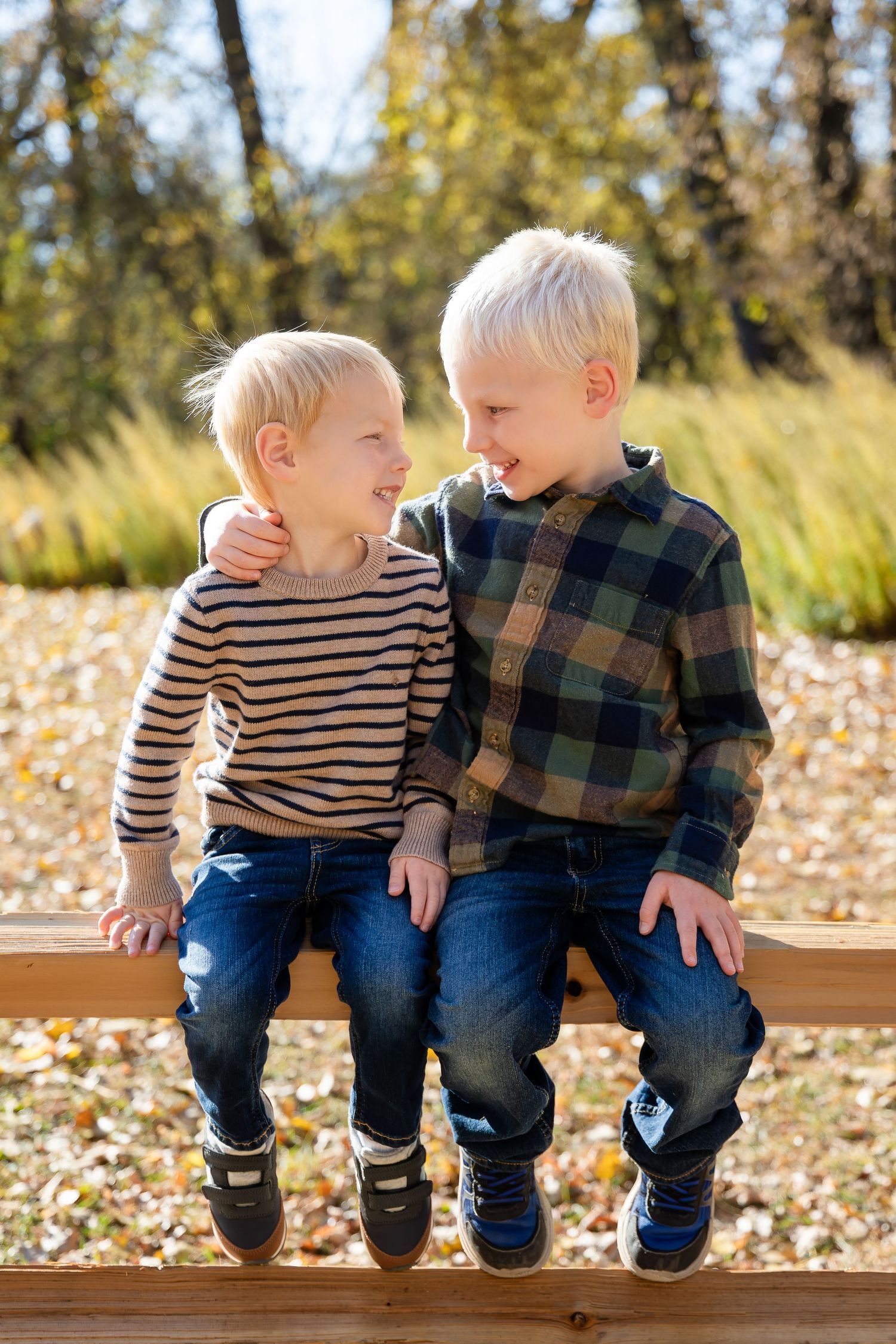 Two children sitting together on wooden bench sharing laughs in autumn setting.