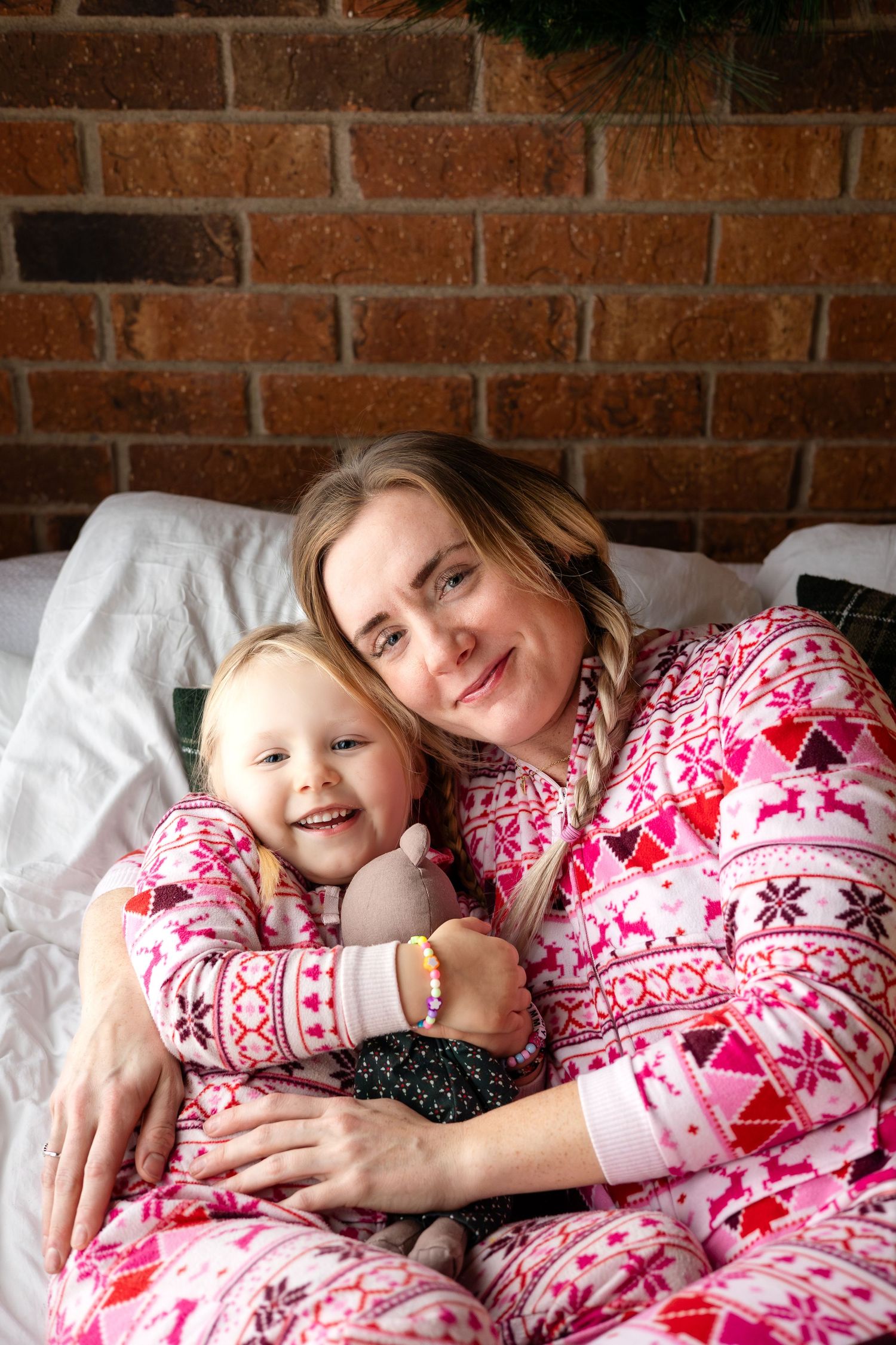 Candid holiday moment showing pink patterned sleepwear against exposed brick wall with wreaths.