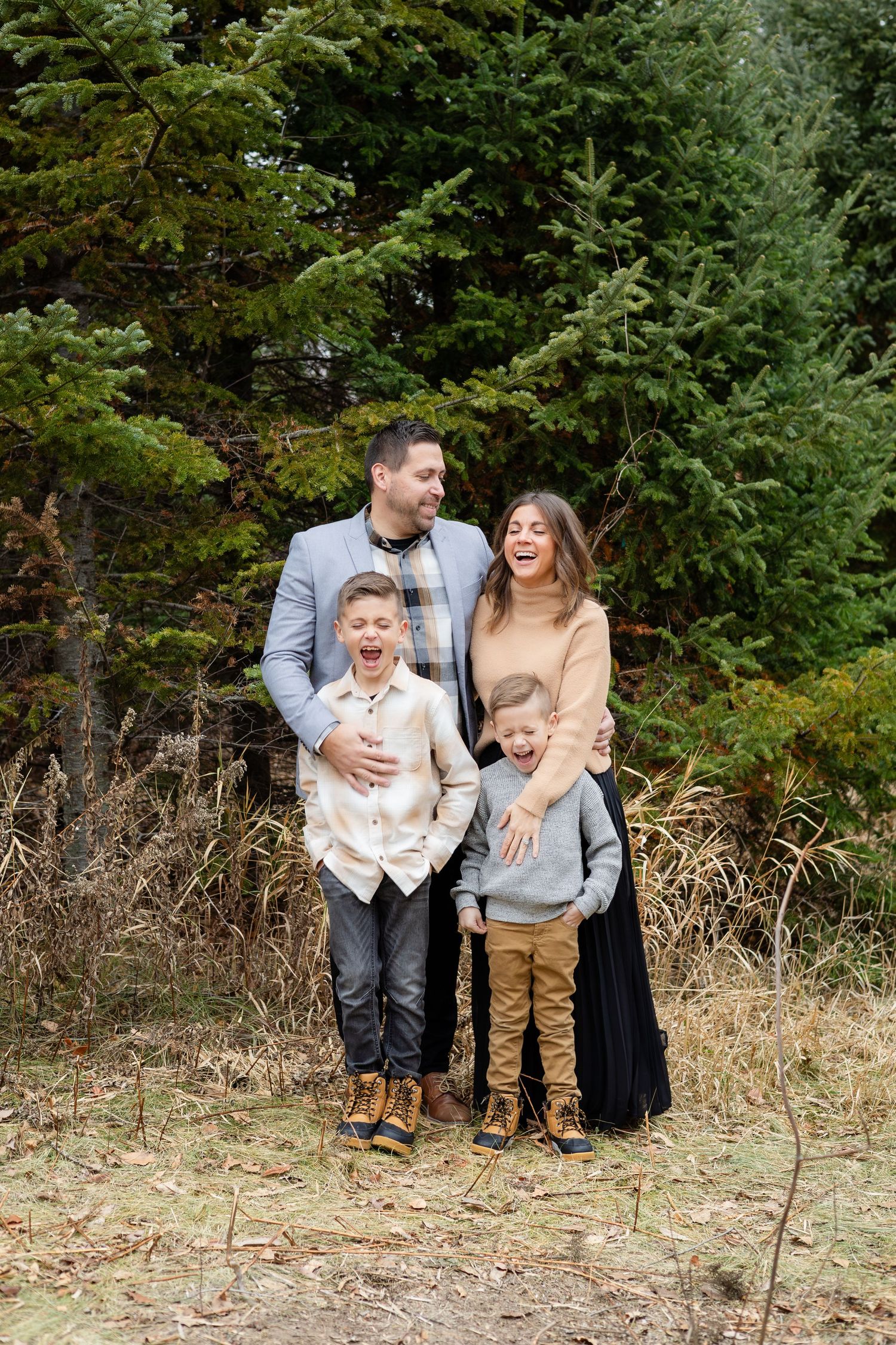 A family group poses playfully in an autumn field with evergreen trees creating a natural backdrop.