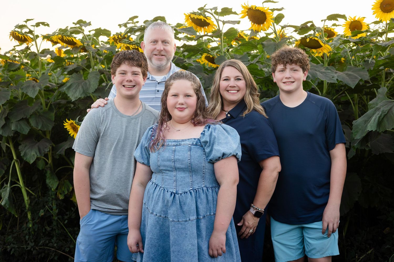 Family gathering in a sunflower field with bright yellow flowers in background.
