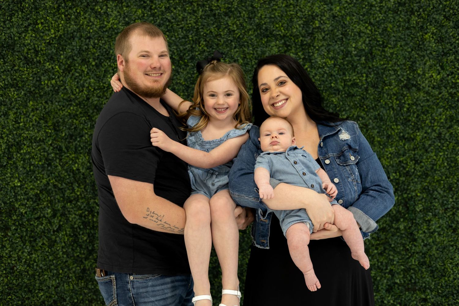A happy family poses together against a green hedge background.
