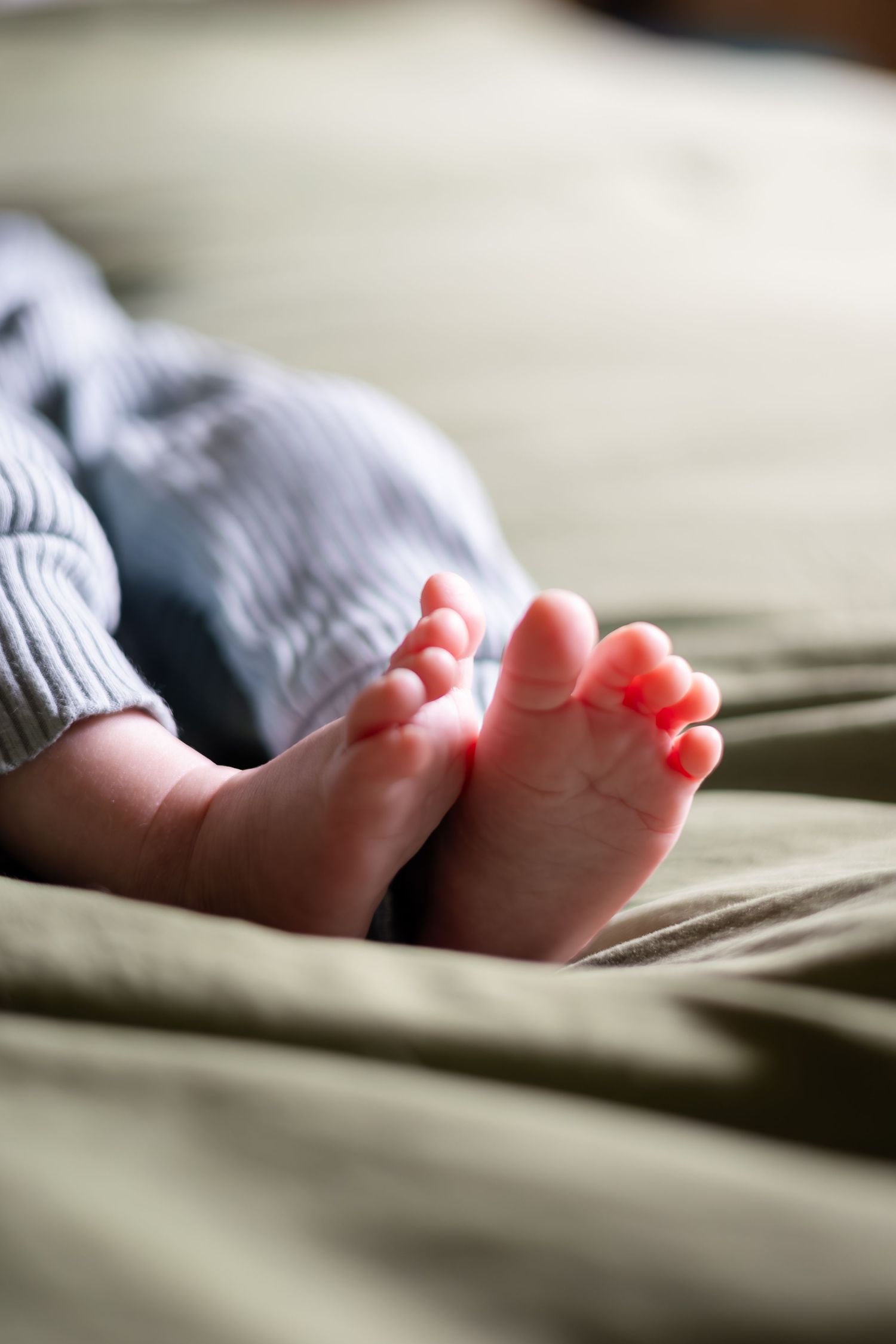 Close-up of tiny baby feet resting on soft bedding in natural light.