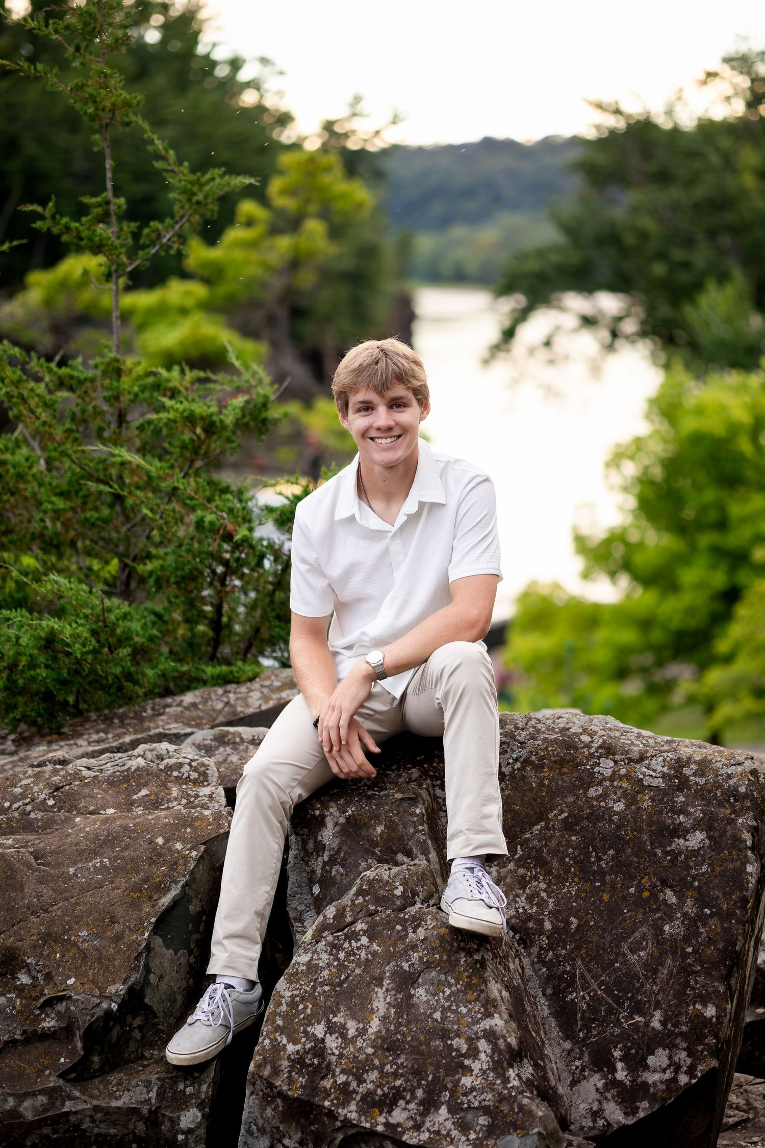 Person in white polo and khakis relaxes on rocky outcrop with scenic water view.