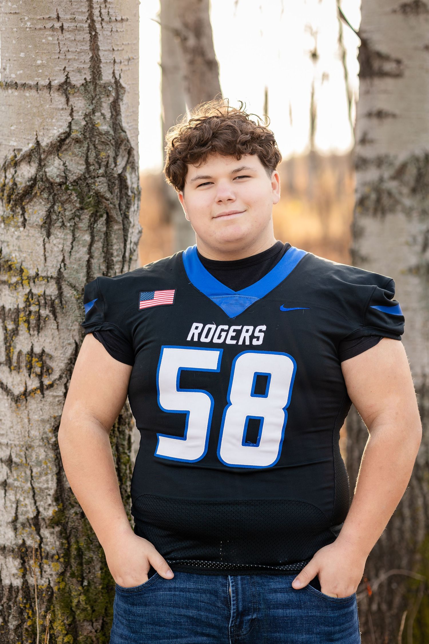 Person wearing Rogers football jersey number 50 posing against white birch trees.