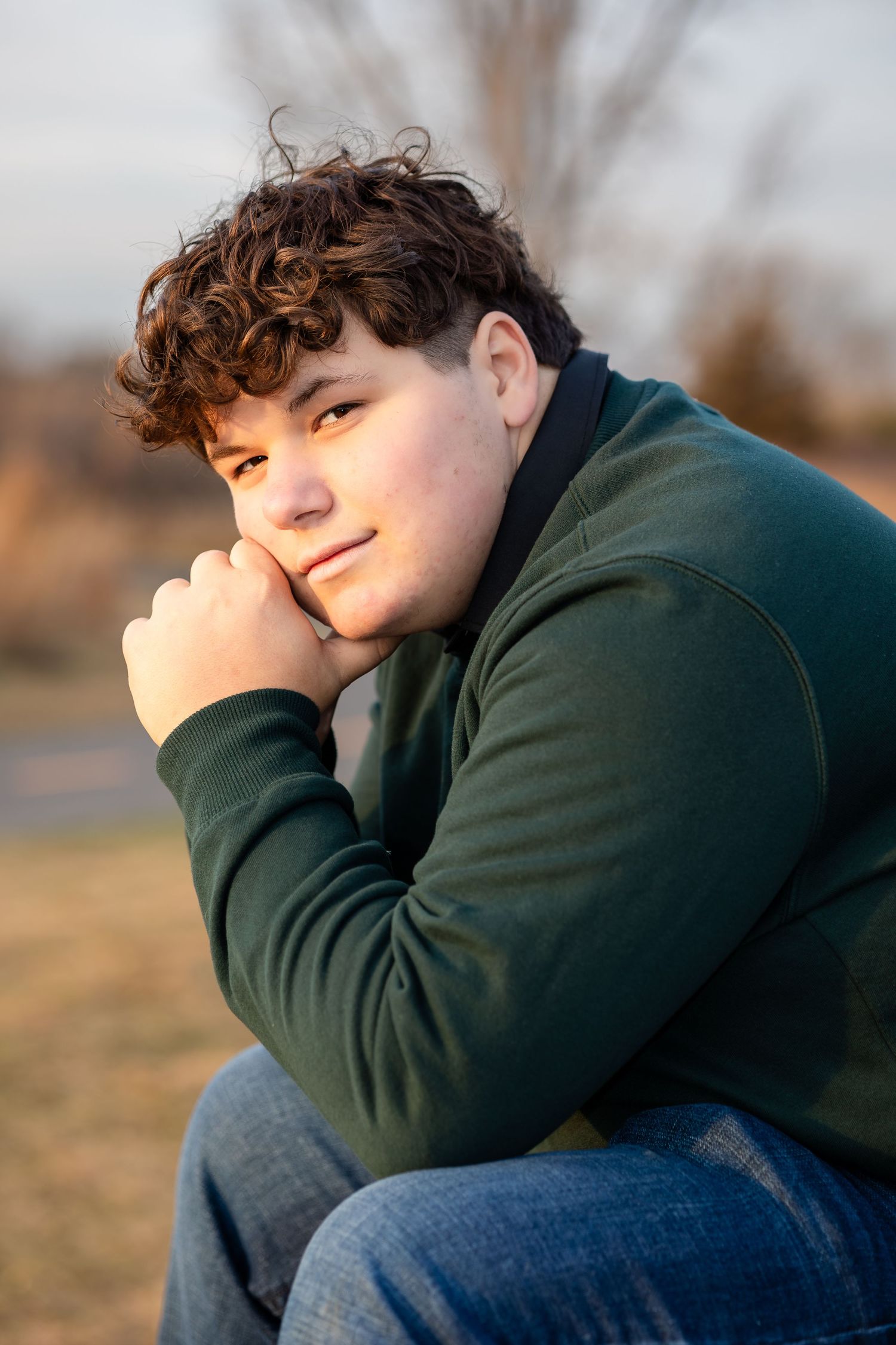 Person in dark hoodie rests head on knee in contemplative outdoor portrait.