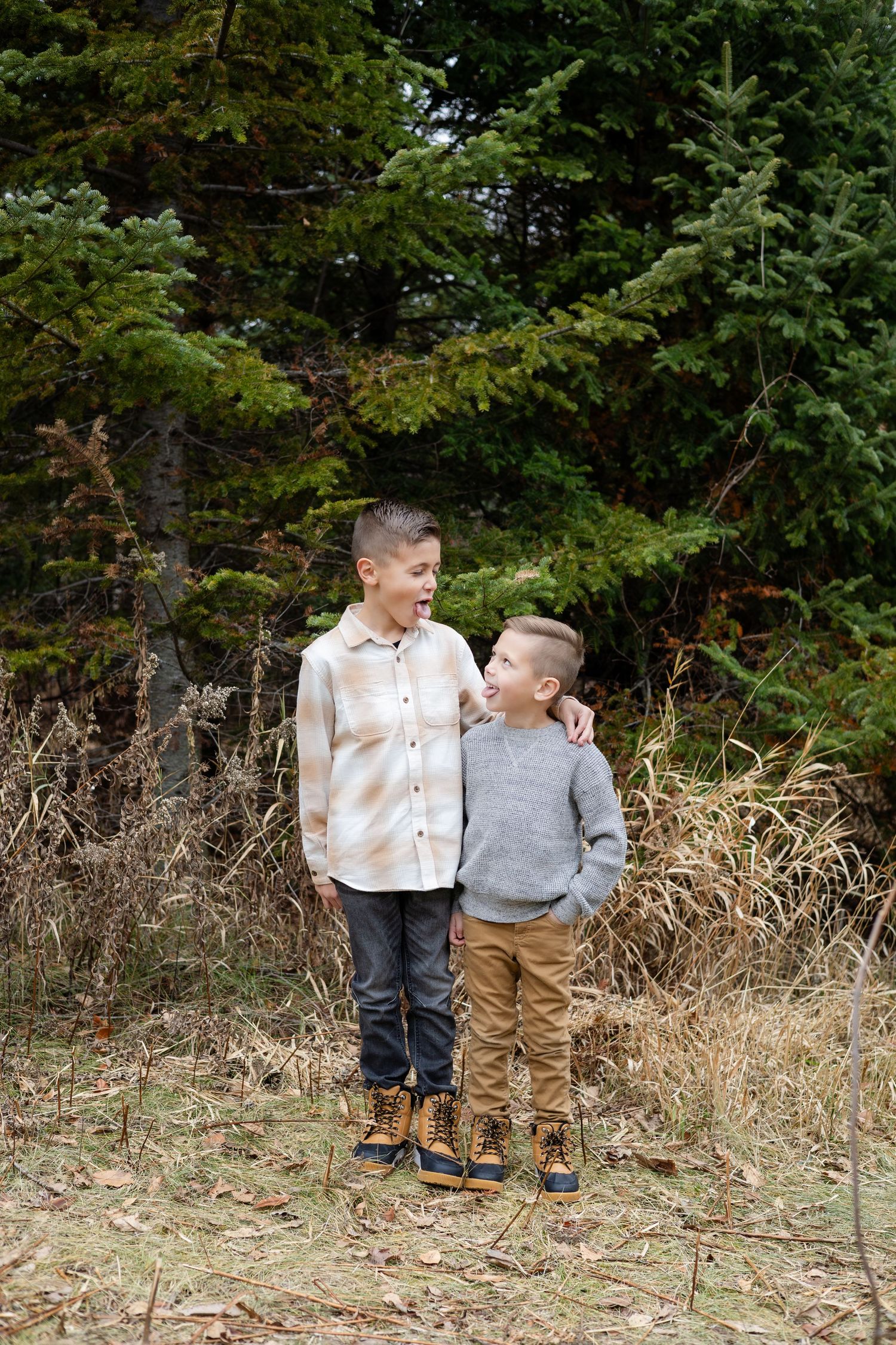 Two young children in casual clothing stand together in a grassy outdoor setting with trees in the background.