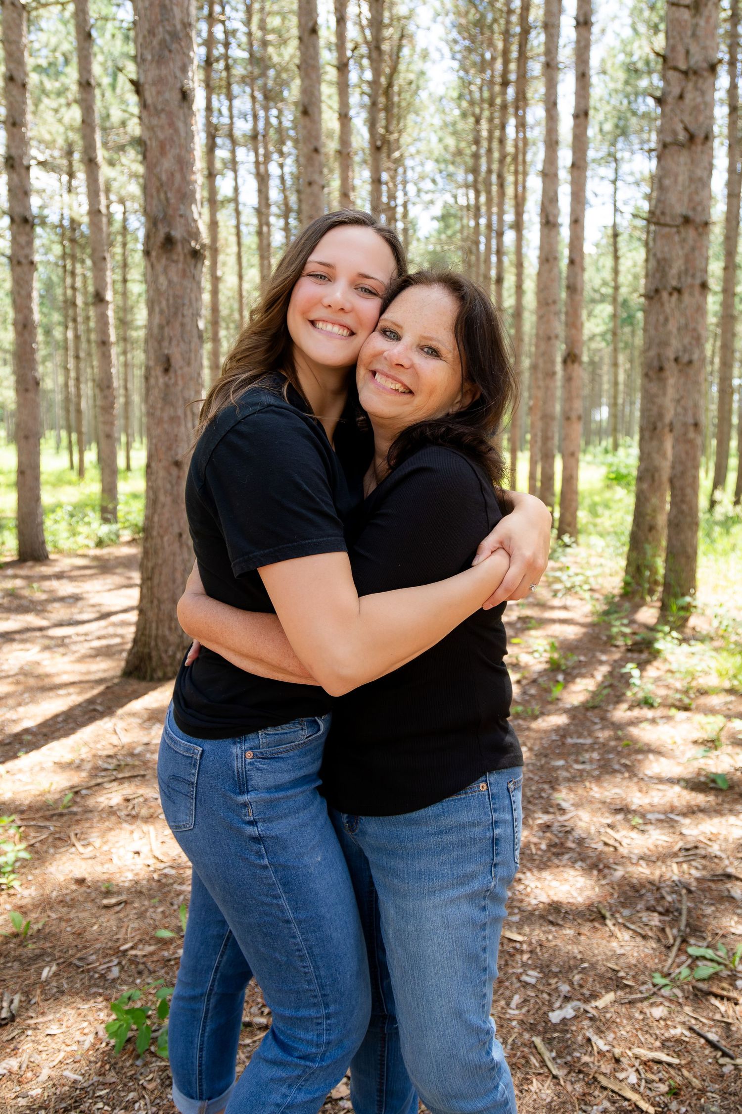 Two people embracing and smiling in sunny pine forest setting.