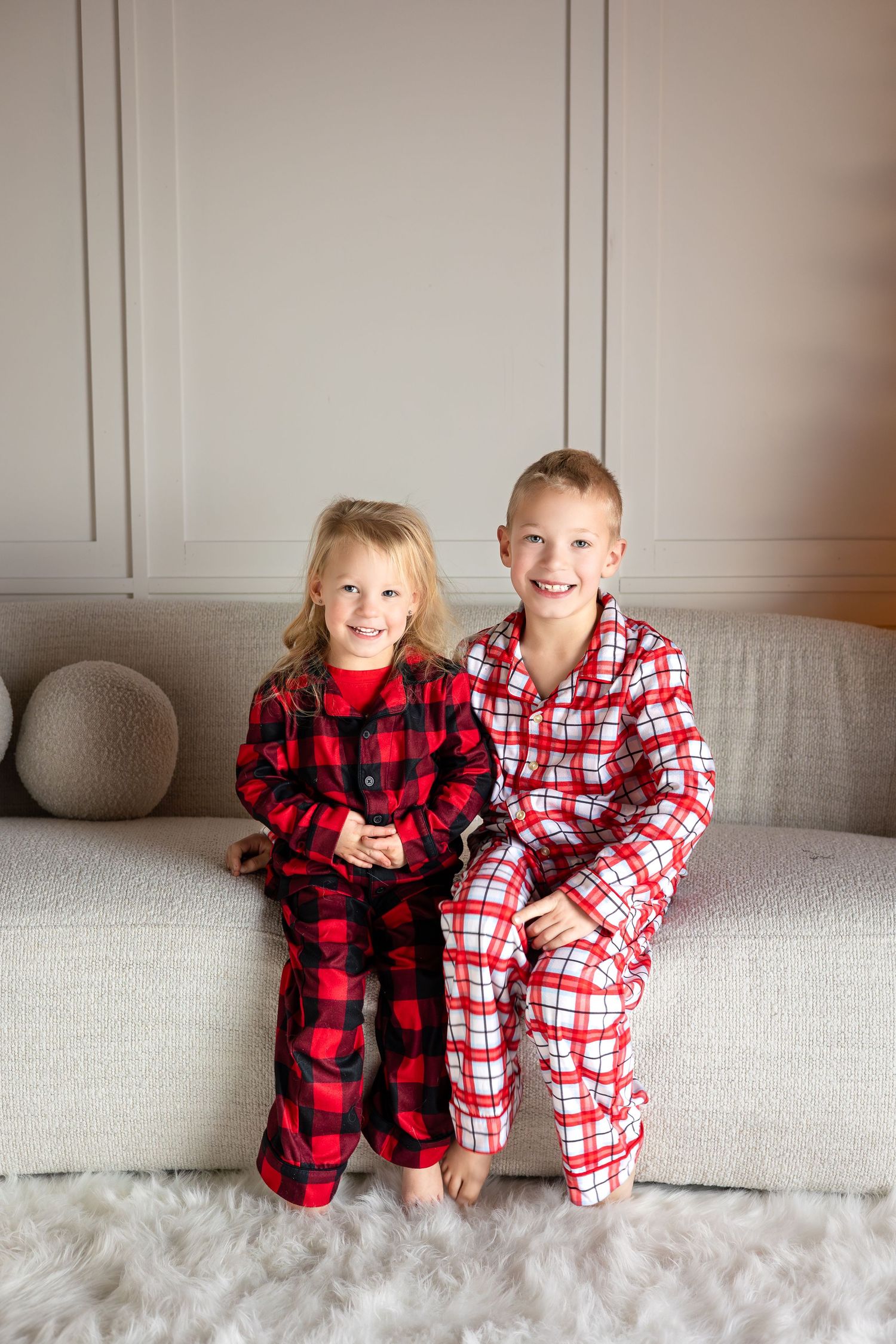 Children in cozy buffalo plaid pajamas sit together on a light gray couch.