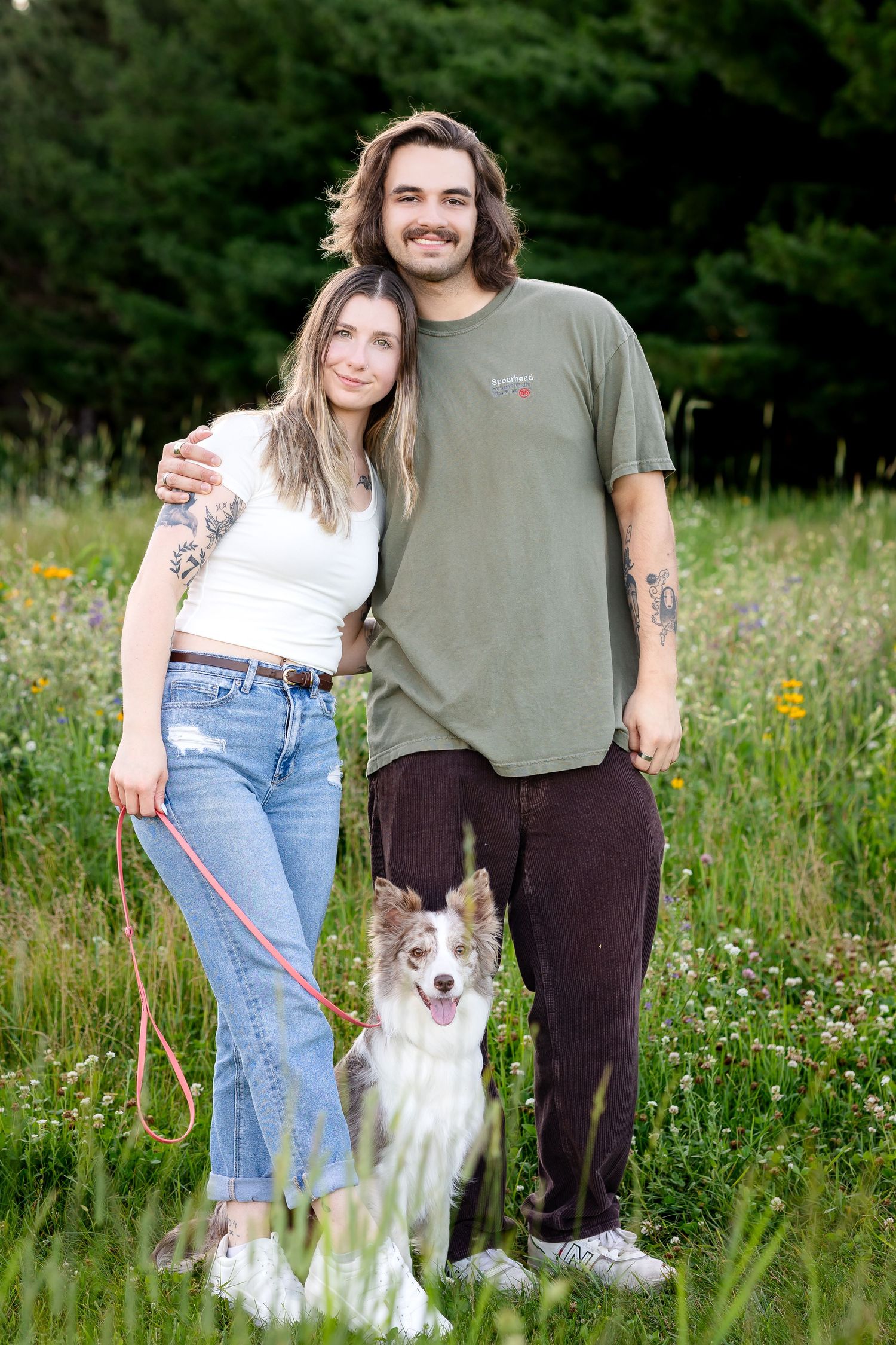 Couple and their border collie dog standing together in a summer meadow.