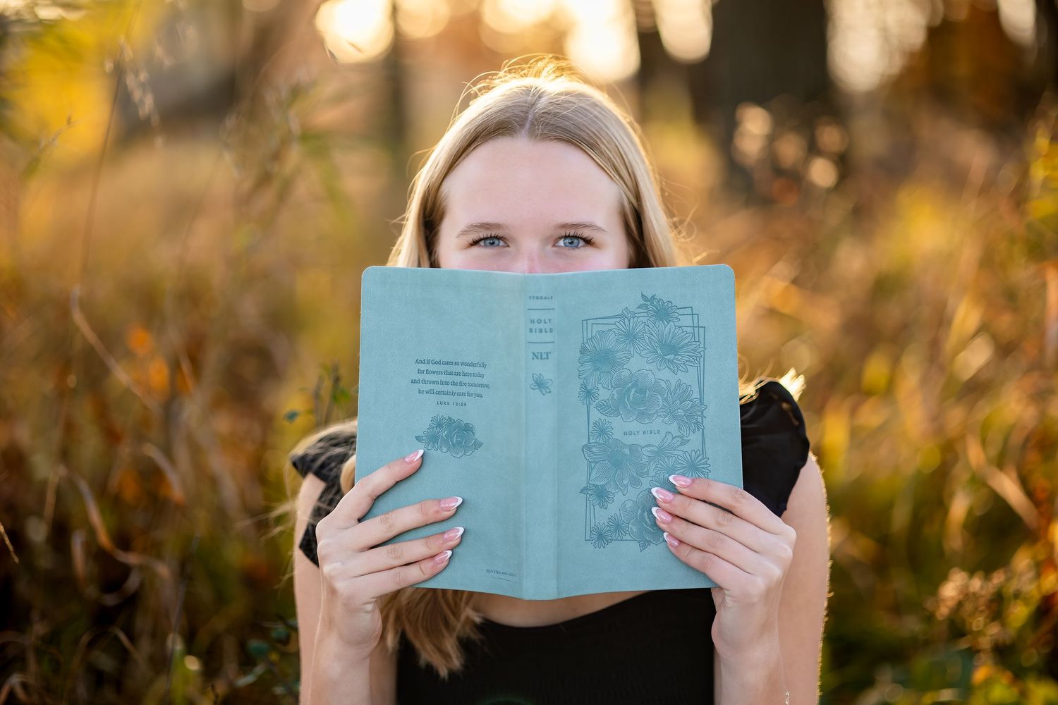 Someone holds up a blue book covering their face against a golden sunset background.