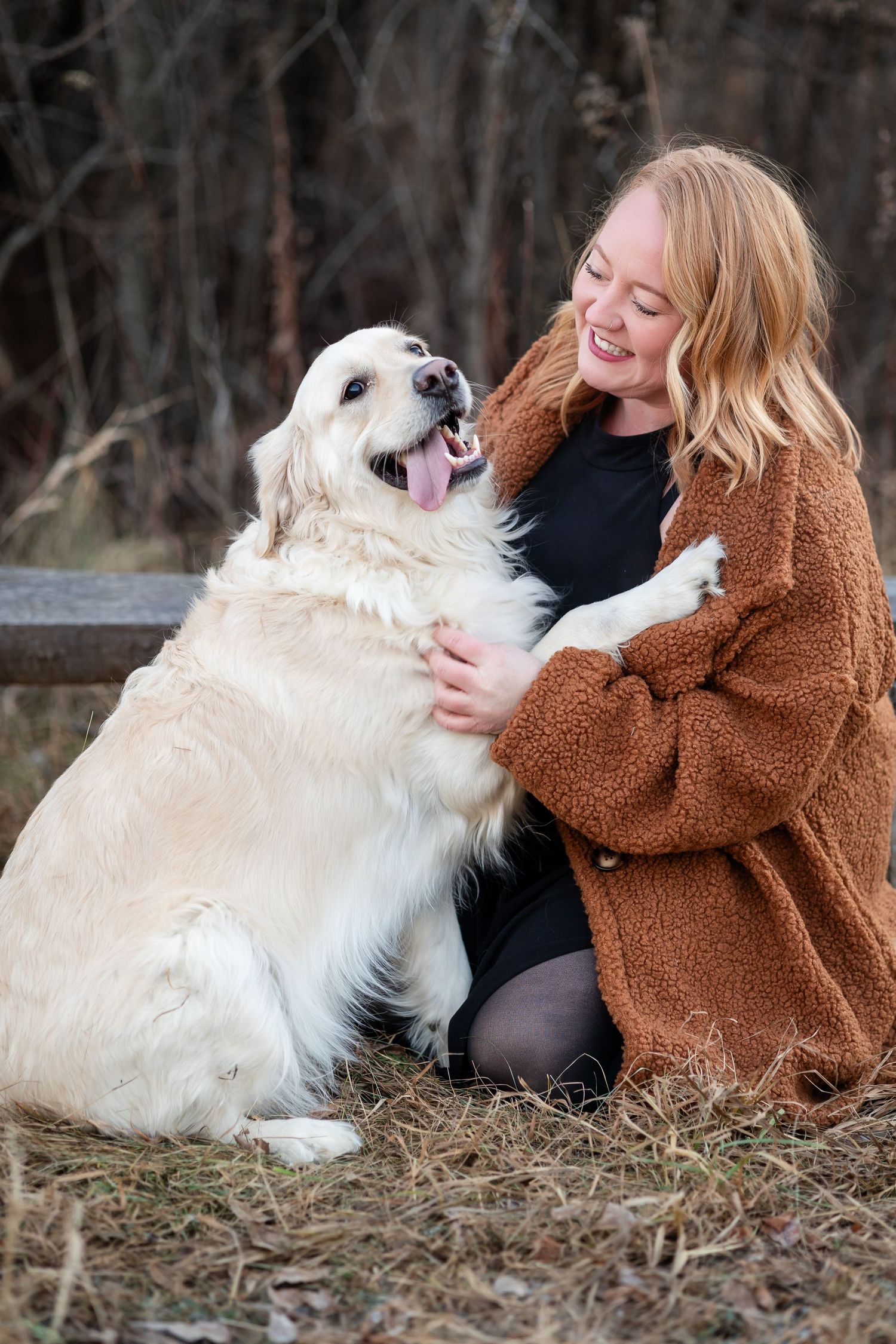 A happy Golden Retriever and person share a joyful moment while sitting outdoors.