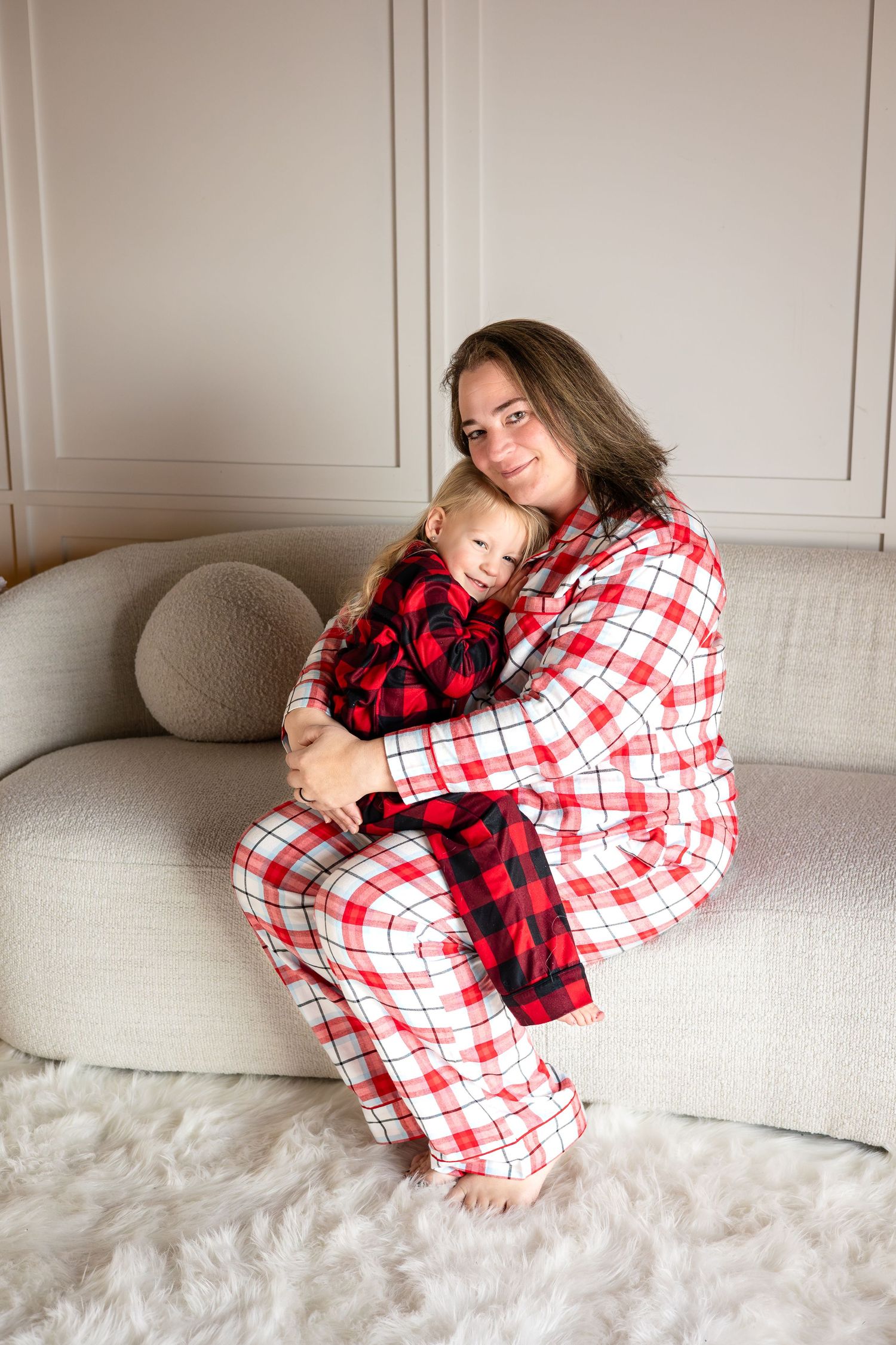 Cozy holiday scene with family in matching plaid pajamas cuddling on gray sofa.