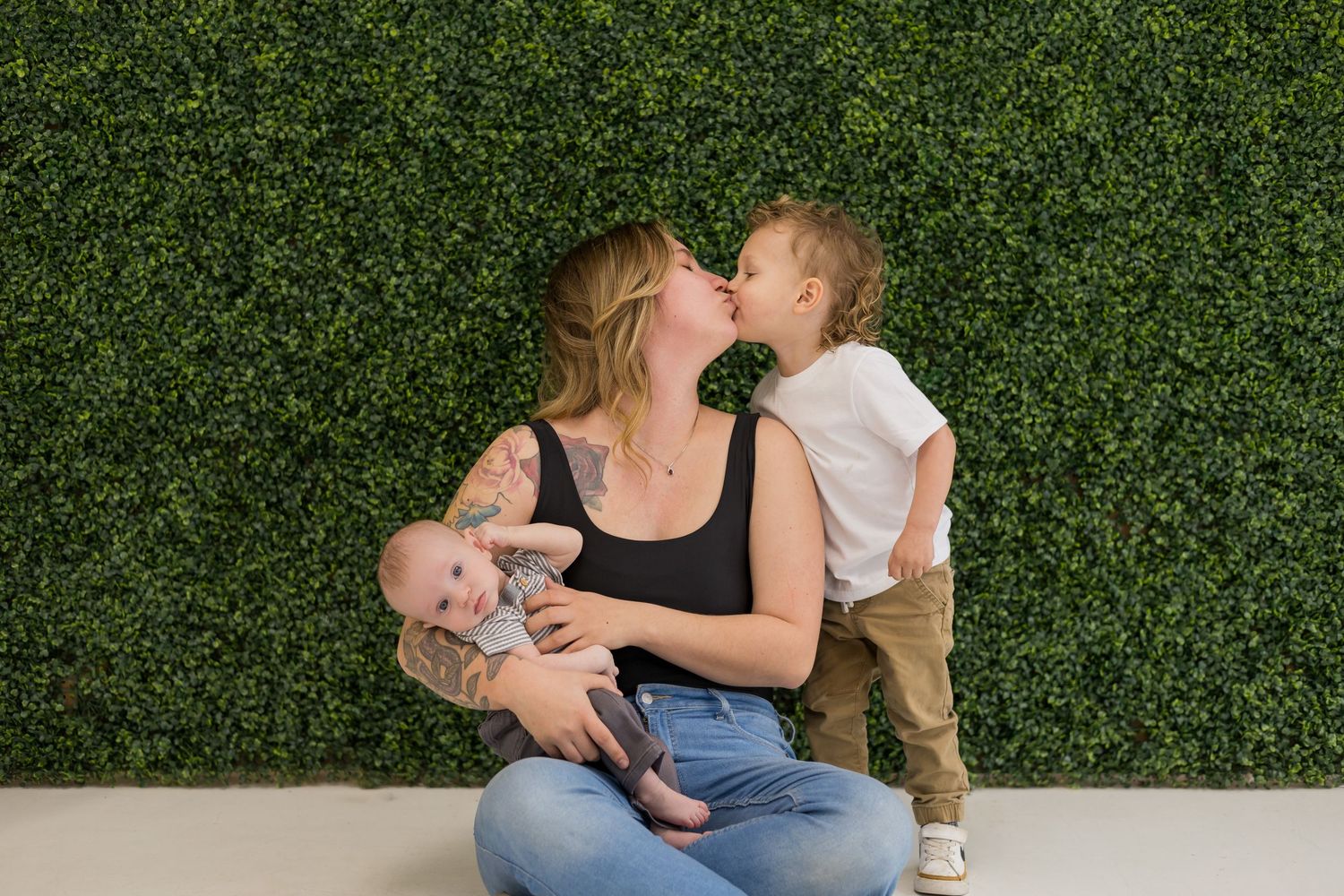 A series of casual family portraits against a decorative green hedge wall.