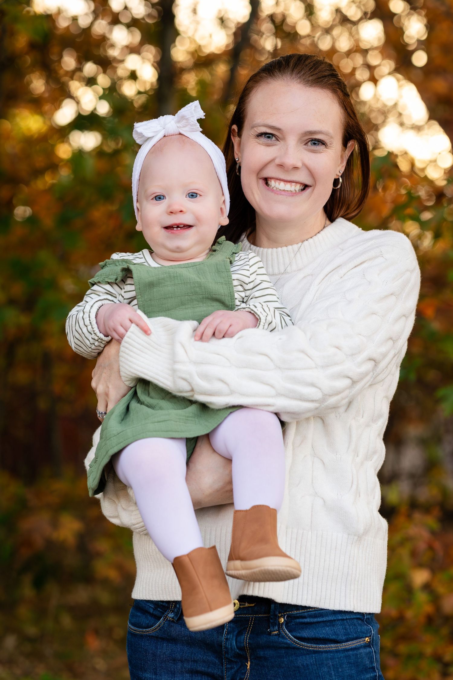 A heartwarming portrait of parent and baby in matching white sweaters against fall foliage.