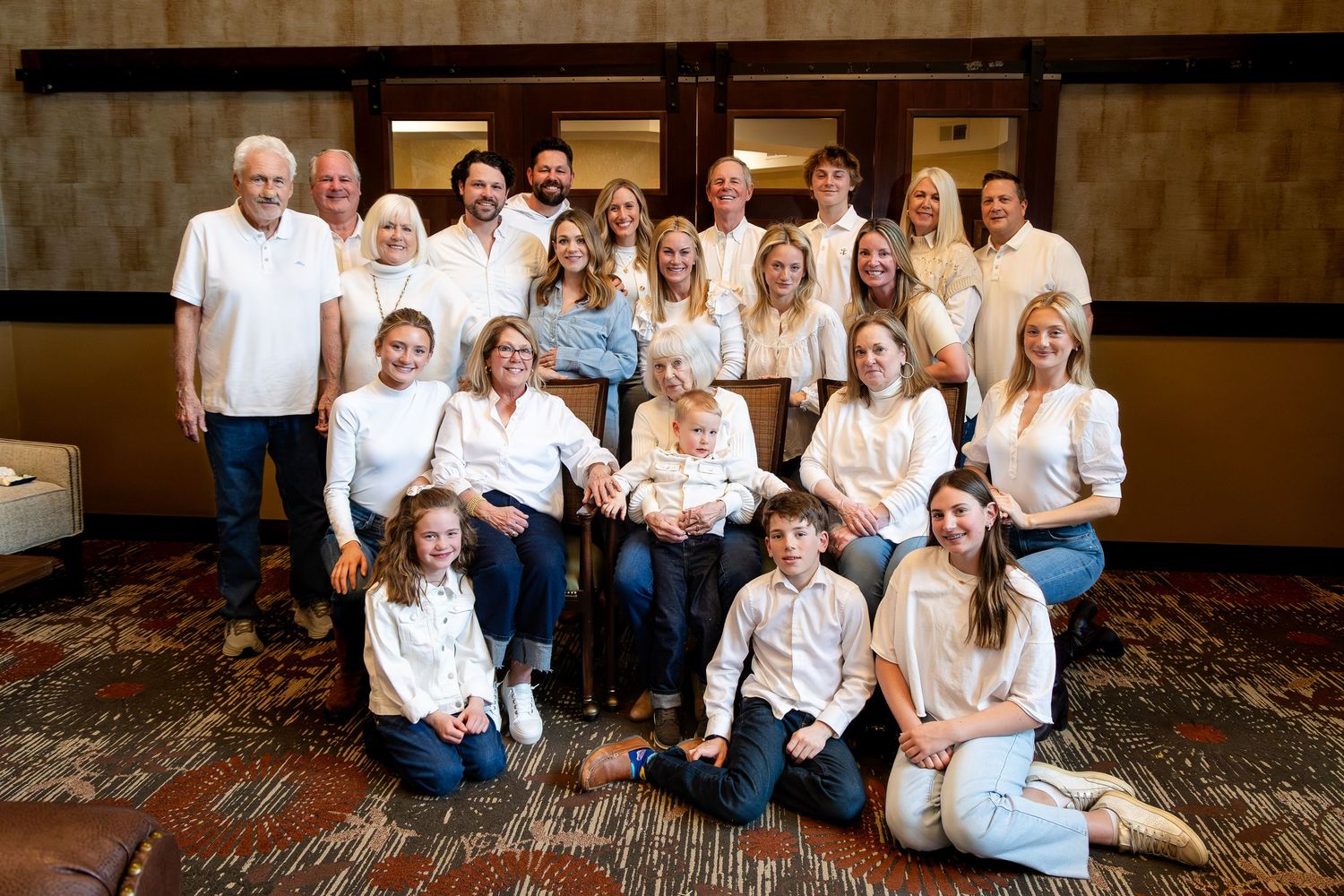Extended family members in matching white shirts and jeans pose together for a formal group portrait.