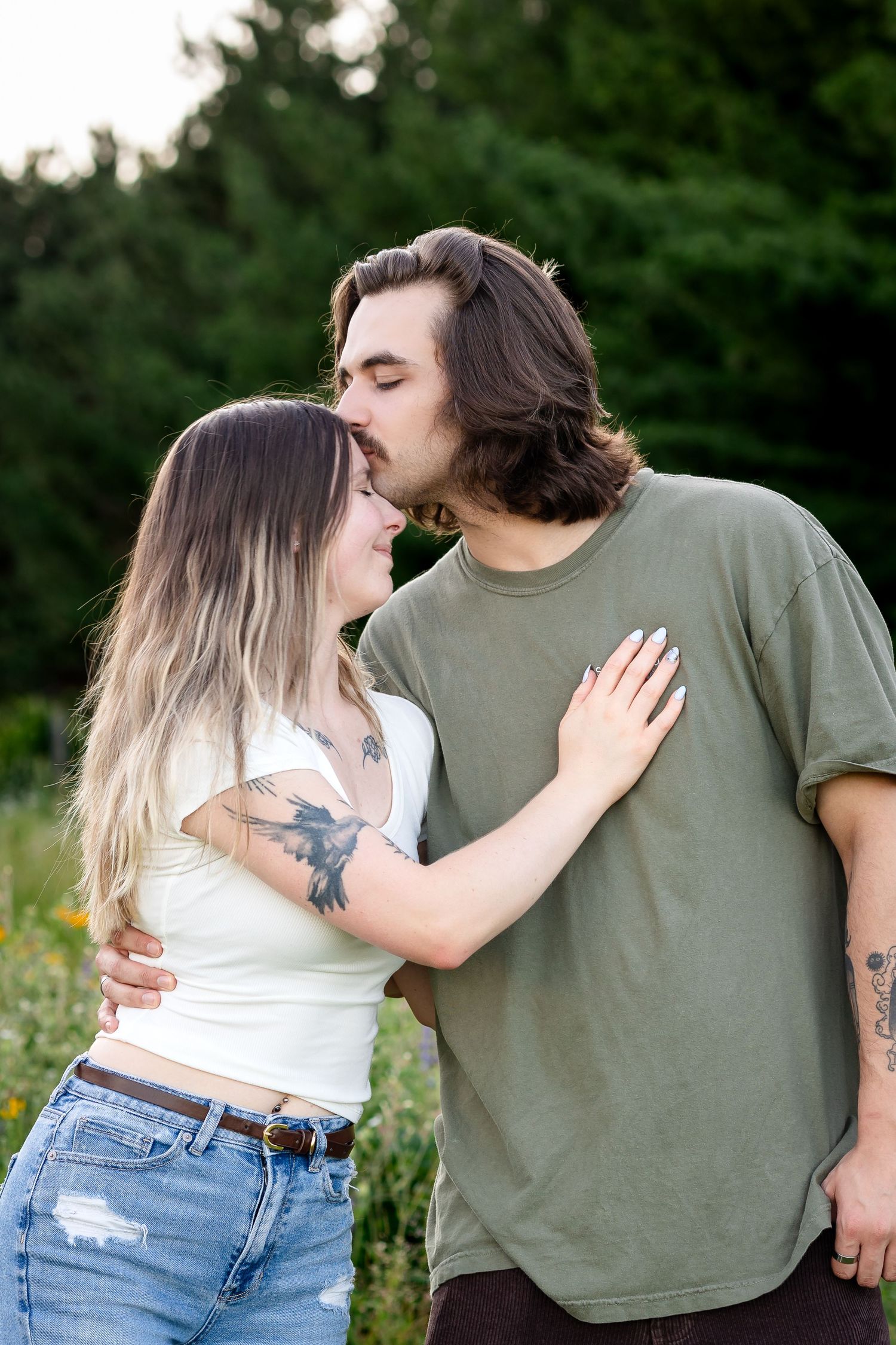 Couple embracing and sharing affectionate moments in a meadow setting.