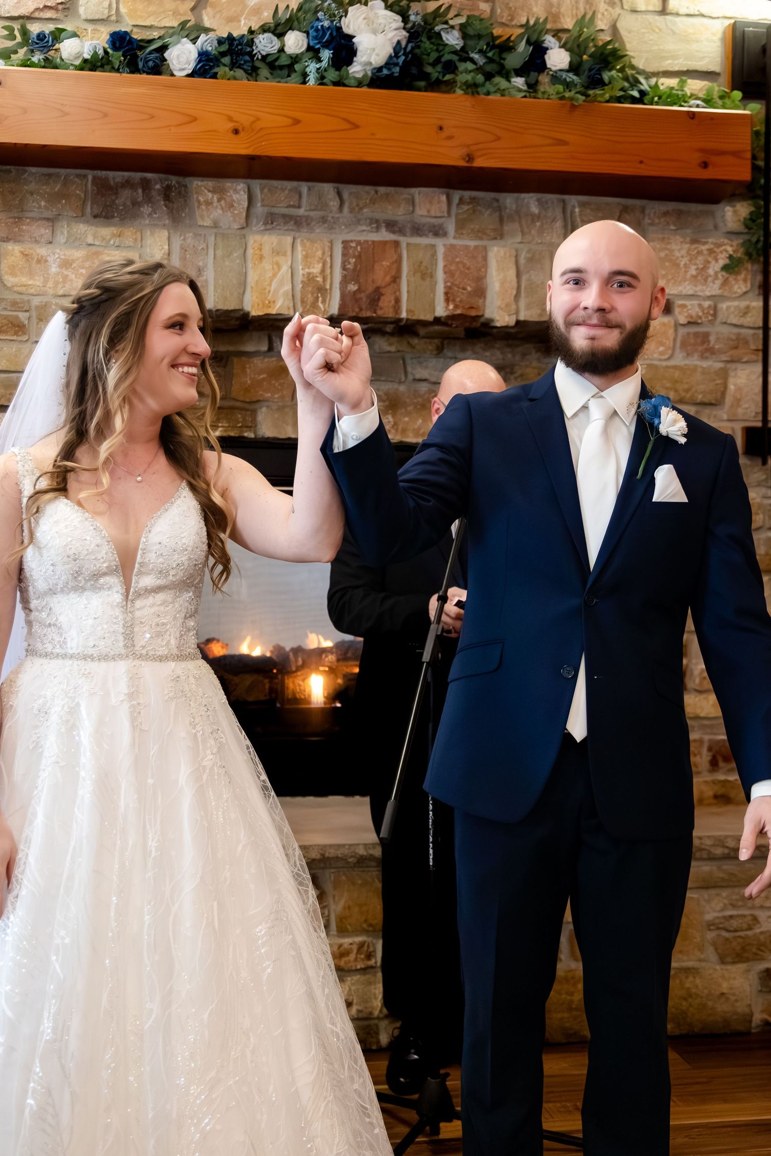 Bride and groom celebrate as newly married couple holding hands before stone fireplace altar.